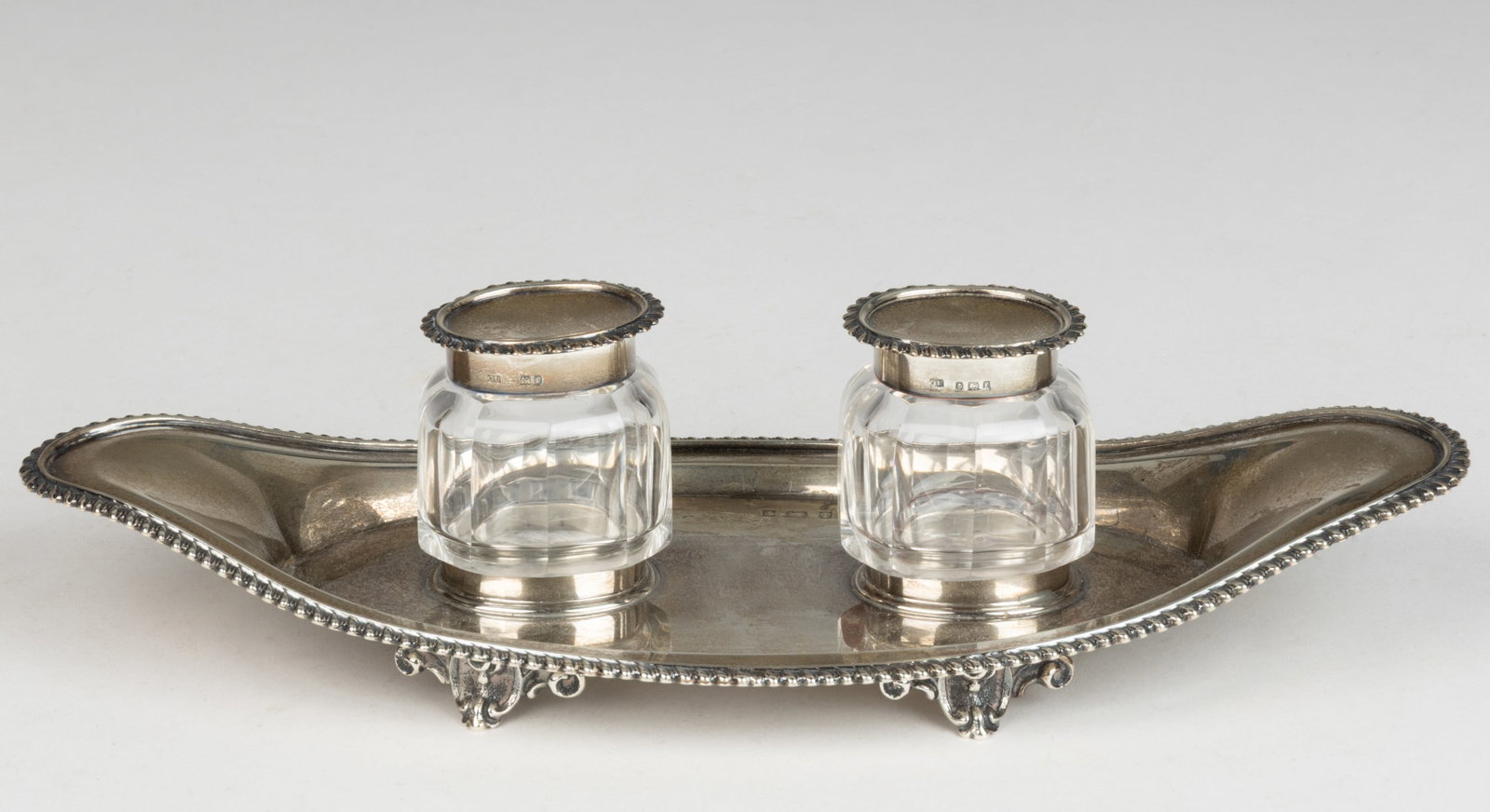 GEORGE UNITE & SONS, ENGLISH EDWARDIAN STERLING SILVER INKSTAND: GEORGE UNITE & SONS, ENGLISH EDWARDIAN STERLING SILVER INKSTAND, a boat-form inkstand with two oval holders to center of well, having a gadroon rim and raised on four scroll-accented feet, togethe