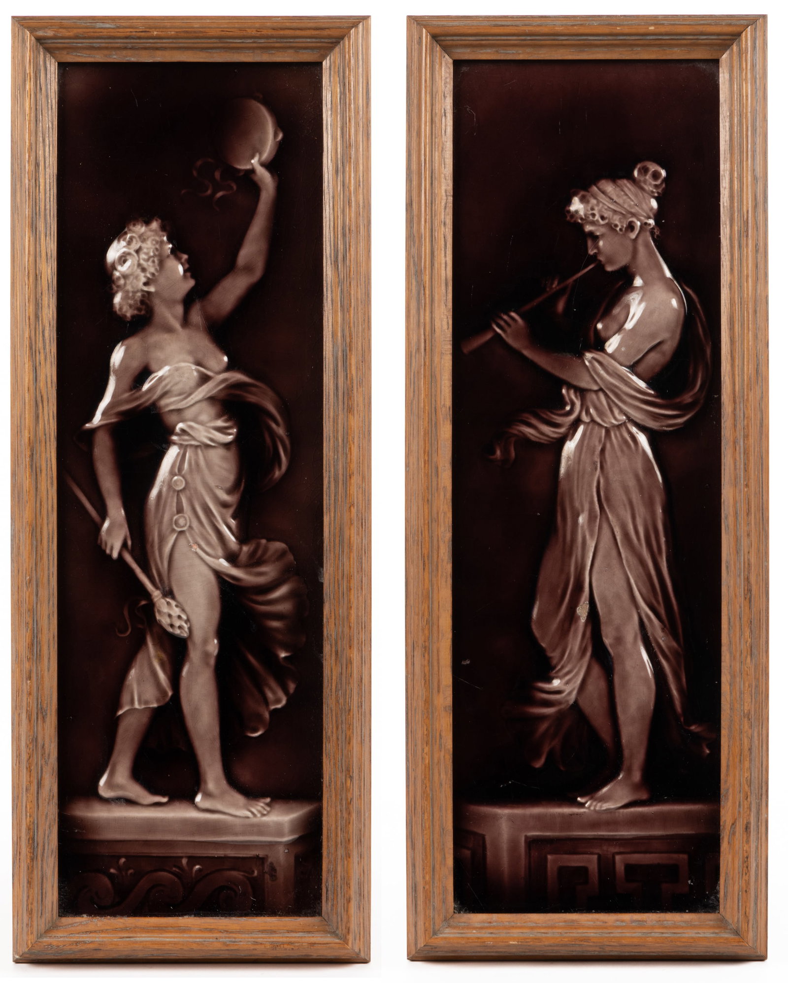 AMERICAN MAJOLICA CERAMIC MUSICIAN MOTIF FRAMED TILE PAIR: AMERICAN MAJOLICA CERAMIC MUSICIAN MOTIF FRAMED TILE PAIR, each of rectangular form with relief decorations depicting young women standing on decorated platforms, comprising one example playing a wood