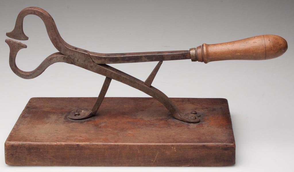 STEEL AND WOODEN SUGAR NIPPERS: STEEL AND WOODEN SUGAR NIPPERS, raised on two legs terminating in heart-shape feet, mounted to a wooden slab base. 19th century. 13 3/4" L, 11" x 6" base.