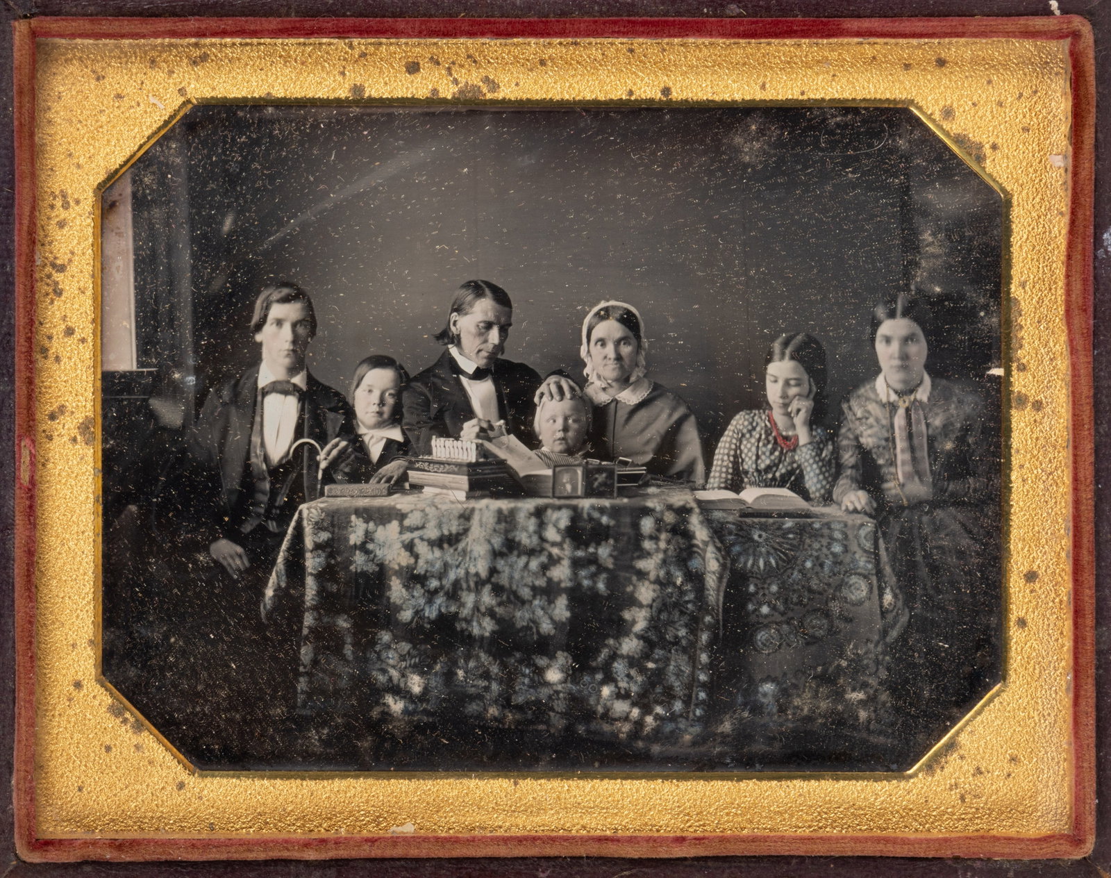 UNIDENTIFIED FAMILY HALF-PLATE DAGUERREOTYPE PHOTOGRAPH: UNIDENTIFIED FAMILY HALF-PLATE DAGUERREOTYPE PHOTOGRAPH, depicting a father, mother, two daughters, and three sons seated at a table with fancy coverings, the father holding calipers in one hand while