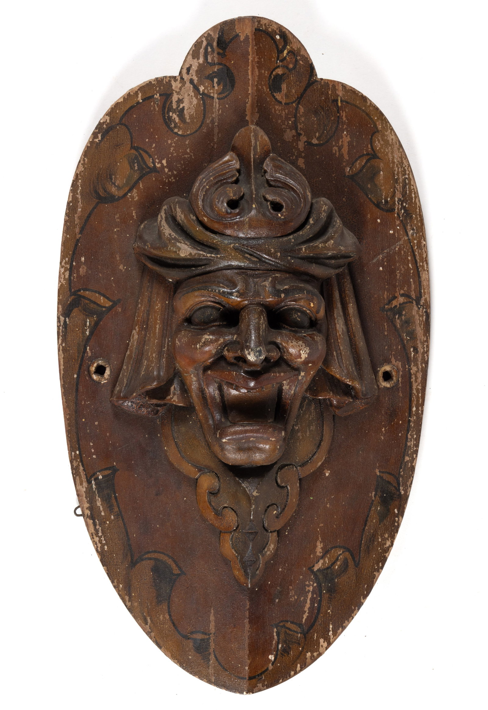 AMERICAN FOLK ART CARVED AND PAINTED CAROUSEL ROUNDING BOARD: AMERICAN FOLK ART CARVED AND PAINTED CAROUSEL ROUNDING BOARD, oval shield-shaped back with carved laughing jester face, entire piece is painted brown with black scrollwork and feathering around the ed