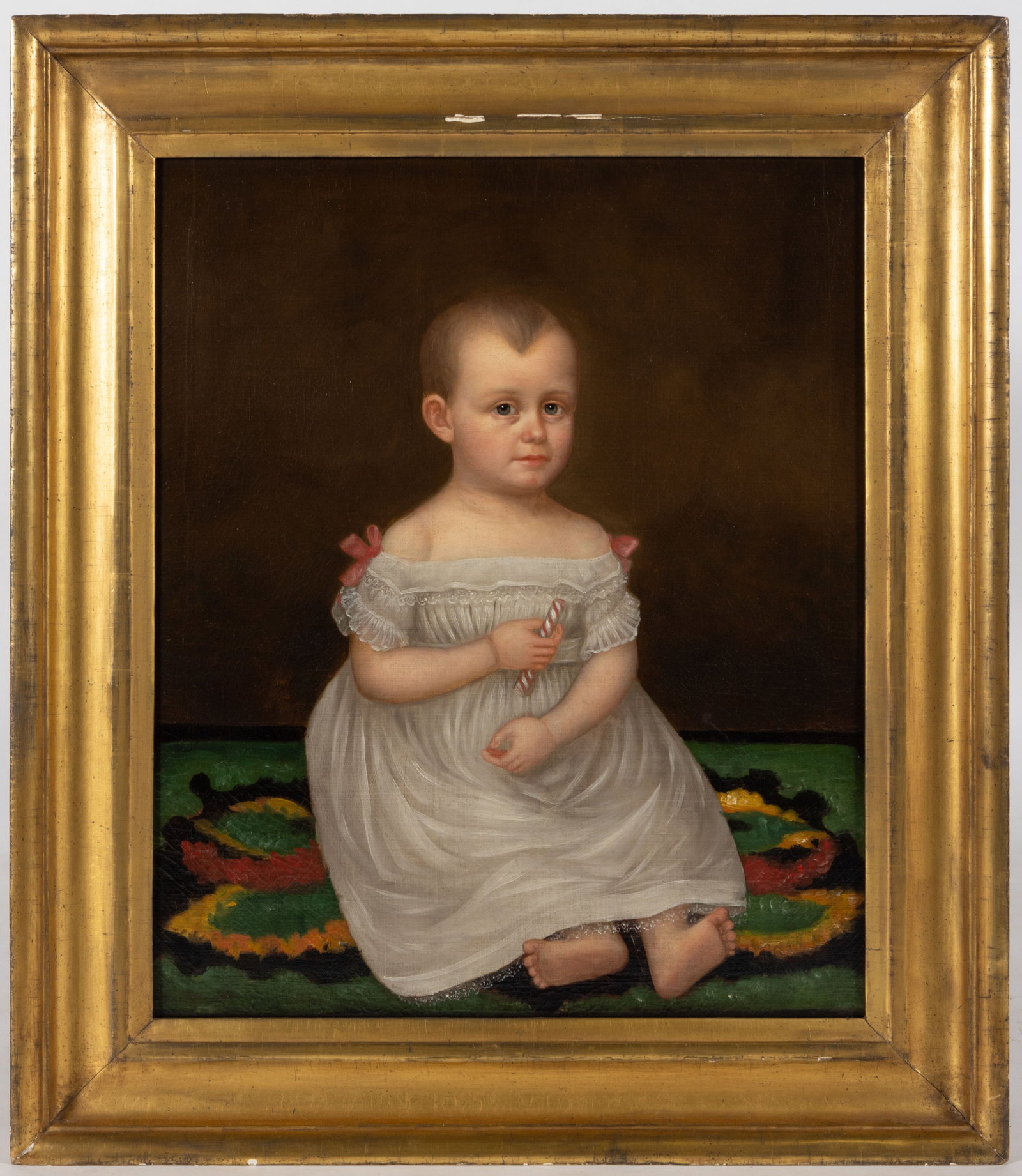 AMERICAN SCHOOL (19TH CENTURY) FOLK ART PORTRAIT OF A CHILD: AMERICAN SCHOOL (19TH CENTURY) FOLK ART PORTRAIT OF A CHILD, oil on canvas, a charming example, featuring a barefoot child in a white gown with pink ribbons seated on a patterned carpet and holding a&