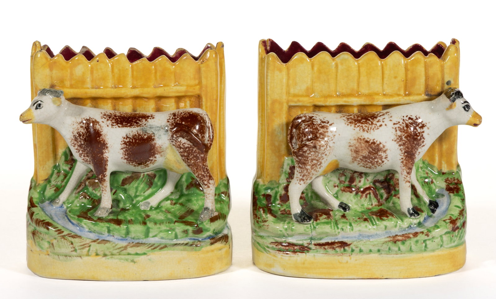 ENGLISH STAFFORDSHIRE HAND-PAINTED CERAMIC COW FIGURAL SPILL VASE PAIR: ENGLISH STAFFORDSHIRE HAND-PAINTED CERAMIC COW FIGURAL SPILL VASE PAIR, having polychrome enamel decorations, each featuring a standing brown-sponged cow in front of a yellow picket fence and bes