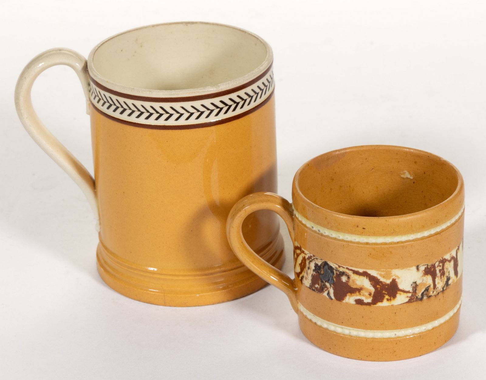 BRITISH / FRENCH DIPPED WARE / MOCHA CERAMIC MUGS, LOT OF TWO: BRITISH / FRENCH DIPPED WARE / MOCHA CERAMIC MUGS, LOT OF TWO, each having brownish yellow ground, comprising one creamware example having a slip-inlaid rouletted herringbone band below the rim a