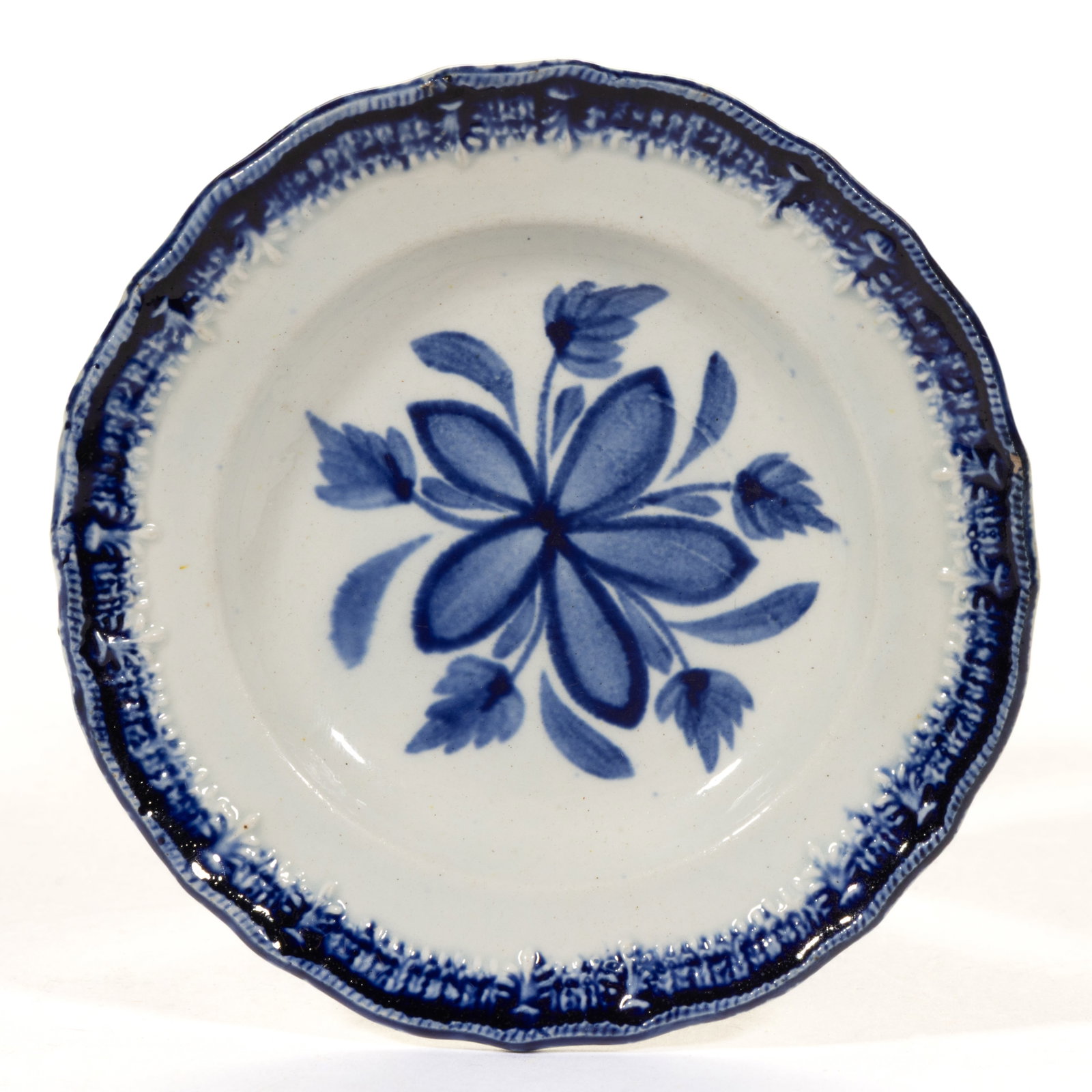 BRITISH PEARLWARE EMBOSSED EDGE HAND-PAINTED FLORAL MOTIF CERAMIC CUP PLATE: BRITISH PEARLWARE EMBOSSED EDGE HAND-PAINTED FLORAL MOTIF CERAMIC CUP PLATE, featuring a blue flower to center and blue-painted embossed stylized foliage to rim. Impressed anchor mark to back. Po
