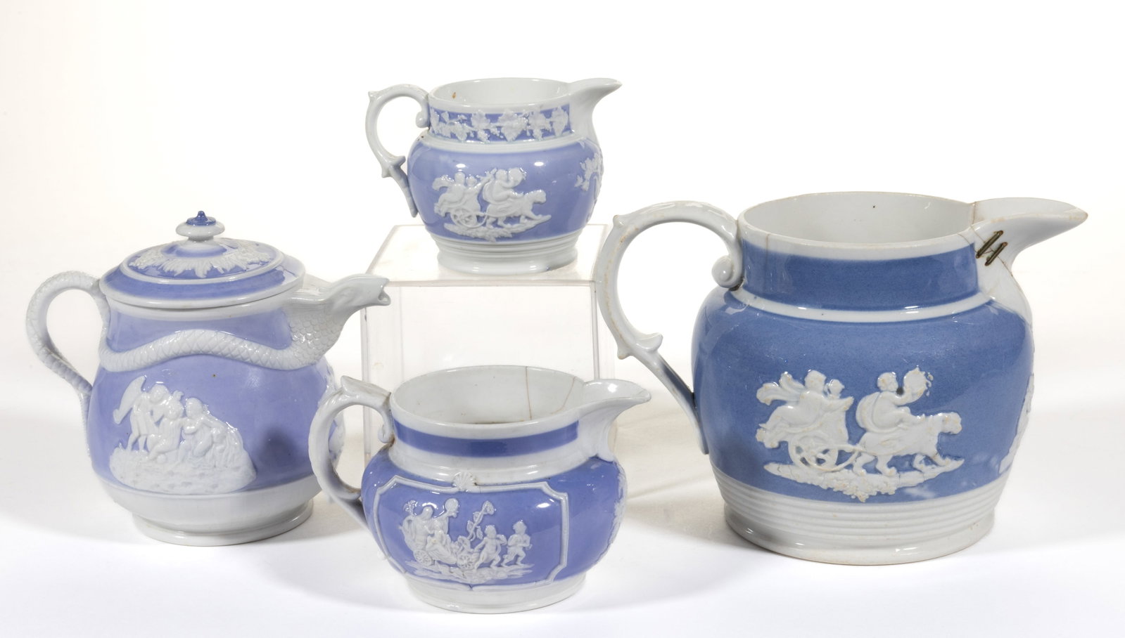 ENGLISH BLUE AND WHITE RELIEF-MOLDED PORCELAIN JUGS / PITCHERS, LOT OF FOUR: ENGLISH BLUE AND WHITE RELIEF-MOLDED PORCELAIN JUGS / PITCHERS, LOT OF FOUR, each featuring neoclassical decorations on blue ground including cherubs being pulled in carts by lions and one covered exa