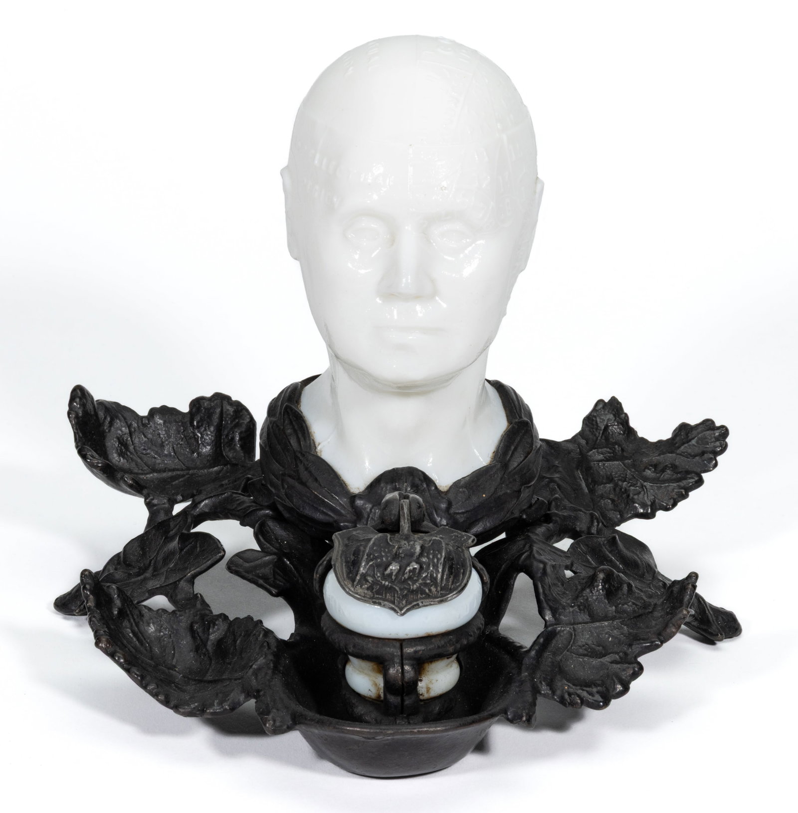 PHRENOLOGIST'S HEAD INKWELL: PHRENOLOGIST'S HEAD INKWELL, opaque white/milk glass bust and inkwell, fitted with wreath-like collar and supported by a metal stand formed as a cluster of leaves and branches. Late 19th/earl