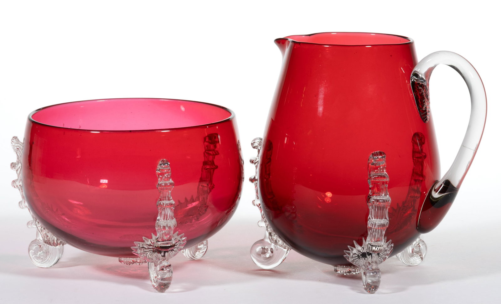 NORTHWOOD LEIGHTON GLASS ARTICLES, LOT OF TWO: NORTHWOOD LEIGHTON GLASS ARTICLES, LOT OF TWO, cranberry, comprising one round bowl and one pitcher, both with three applied colorless reeded scrolled feet and daisy prunts to the underside. H. Northw