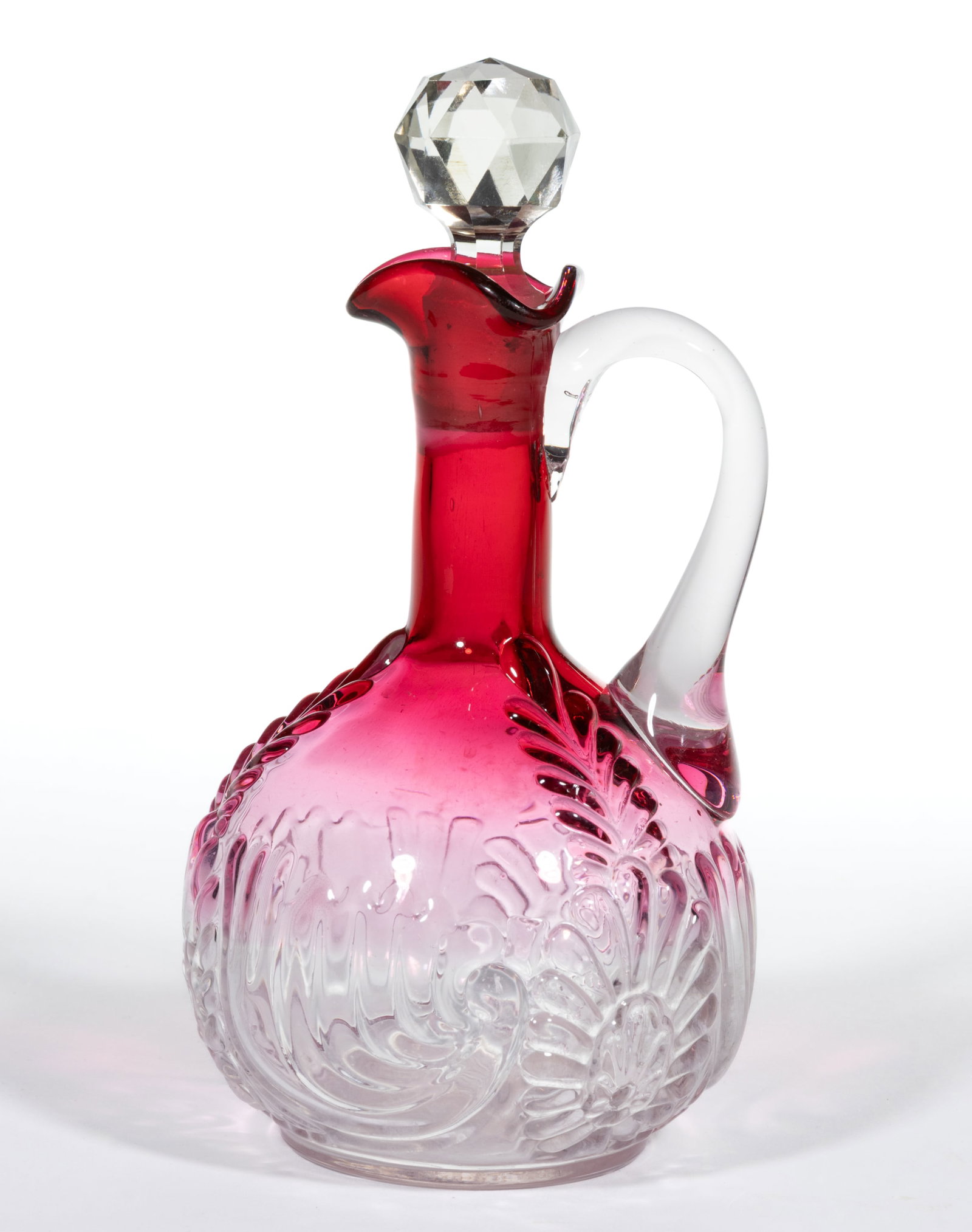 MEDALLION SPRIG CRUET: MEDALLION SPRIG CRUET, cranberry shaded to colorless, tri-fold spout, colorless applied handle, and cut-faceted stopper. West Virginia Glass Co. Circa 1894. 7" HOA. Literature: Parallels Heacock 
