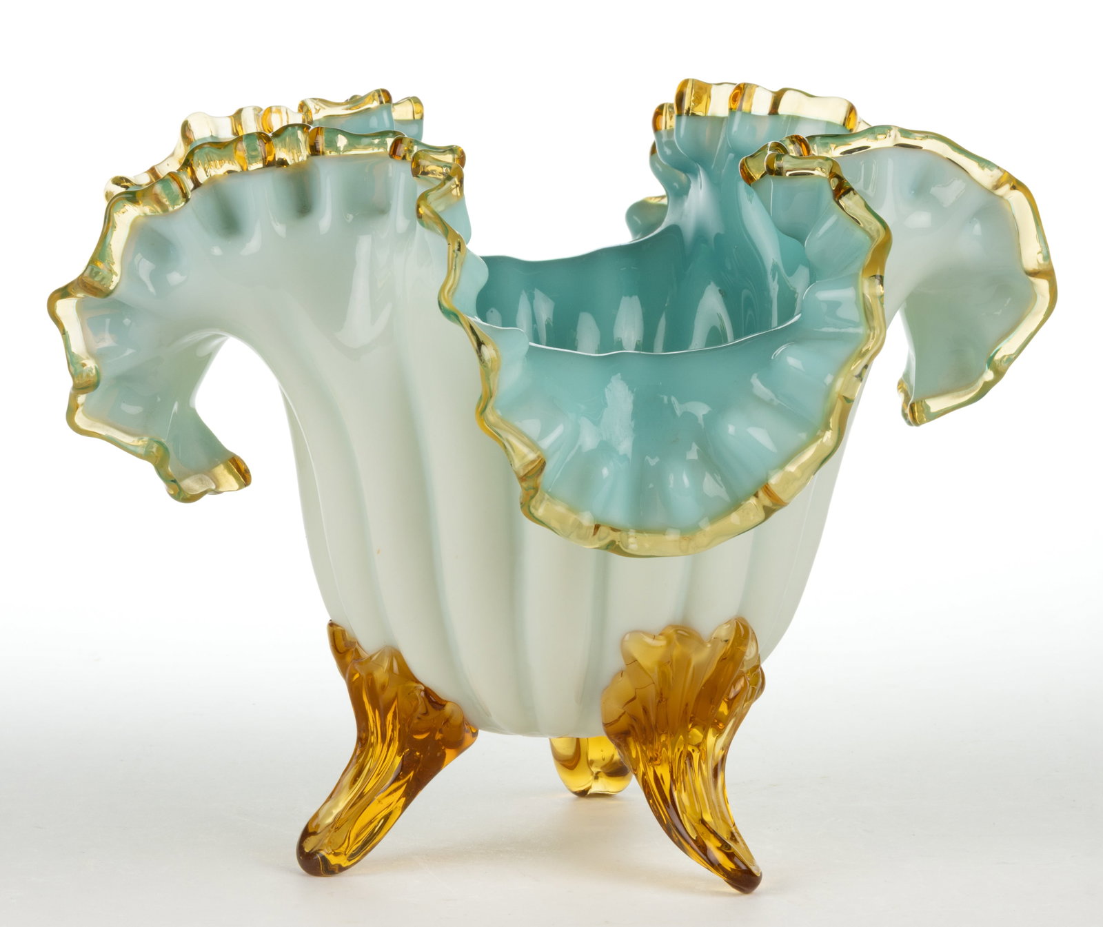 VICTORIAN CASED GLASS FOOTED BOWL: VICTORIAN CASED GLASS FOOTED BOWL, blue cased custard (reacts under black light), 18-lobe form with ruffled-rim, applied amber rim and three feet, polished pontil mark. Maker unverified