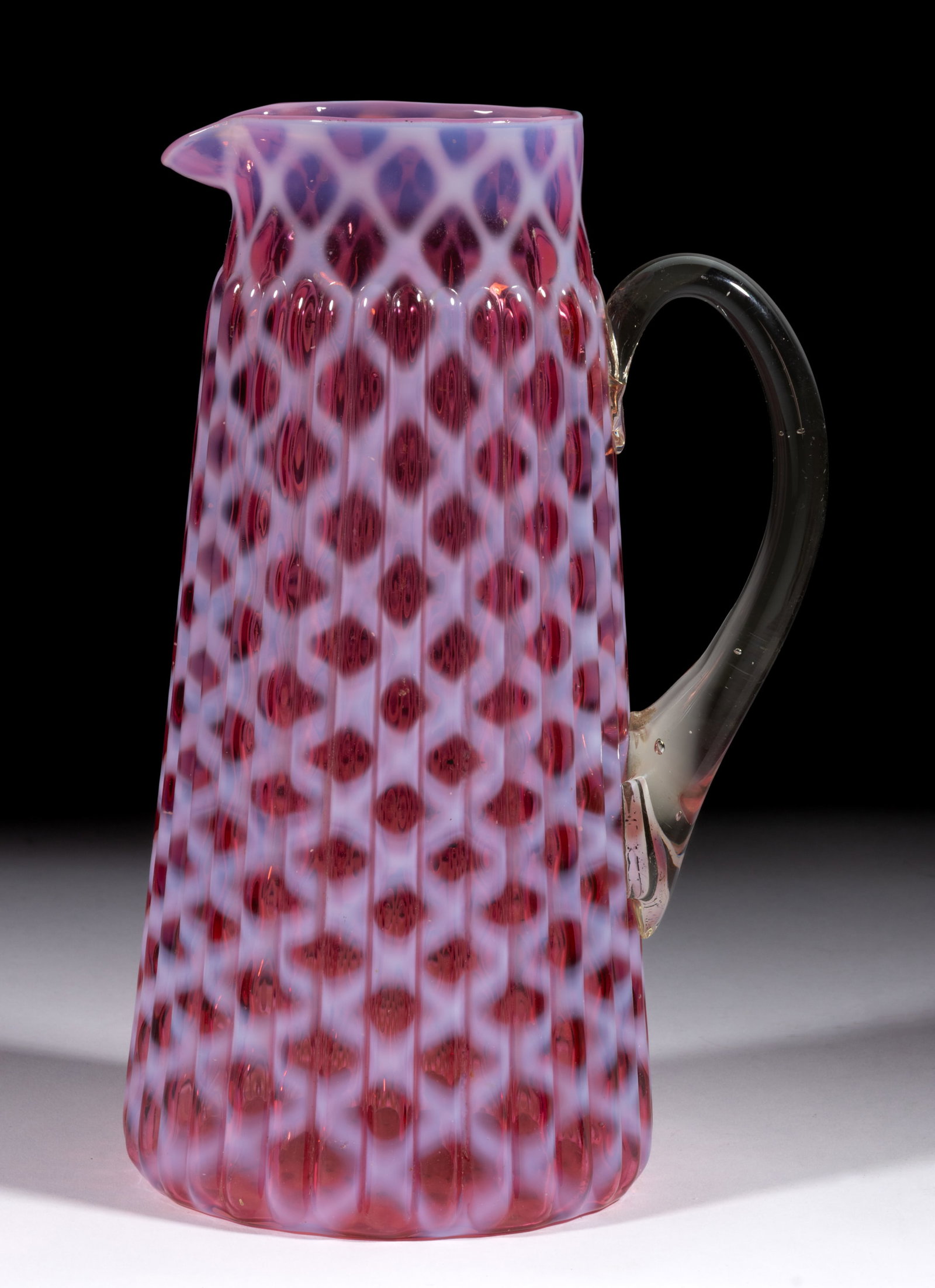 RIBBED OPAL LATTICE TANKARD WATER PITCHER: RIBBED OPAL LATTICE TANKARD WATER PITCHER, cranberry opalescent, with applied colorless handle. H. Northwood Glass Co. Introduced circa 1889. 10 1/4" H, 4" D rim, 5" D base. Literature: