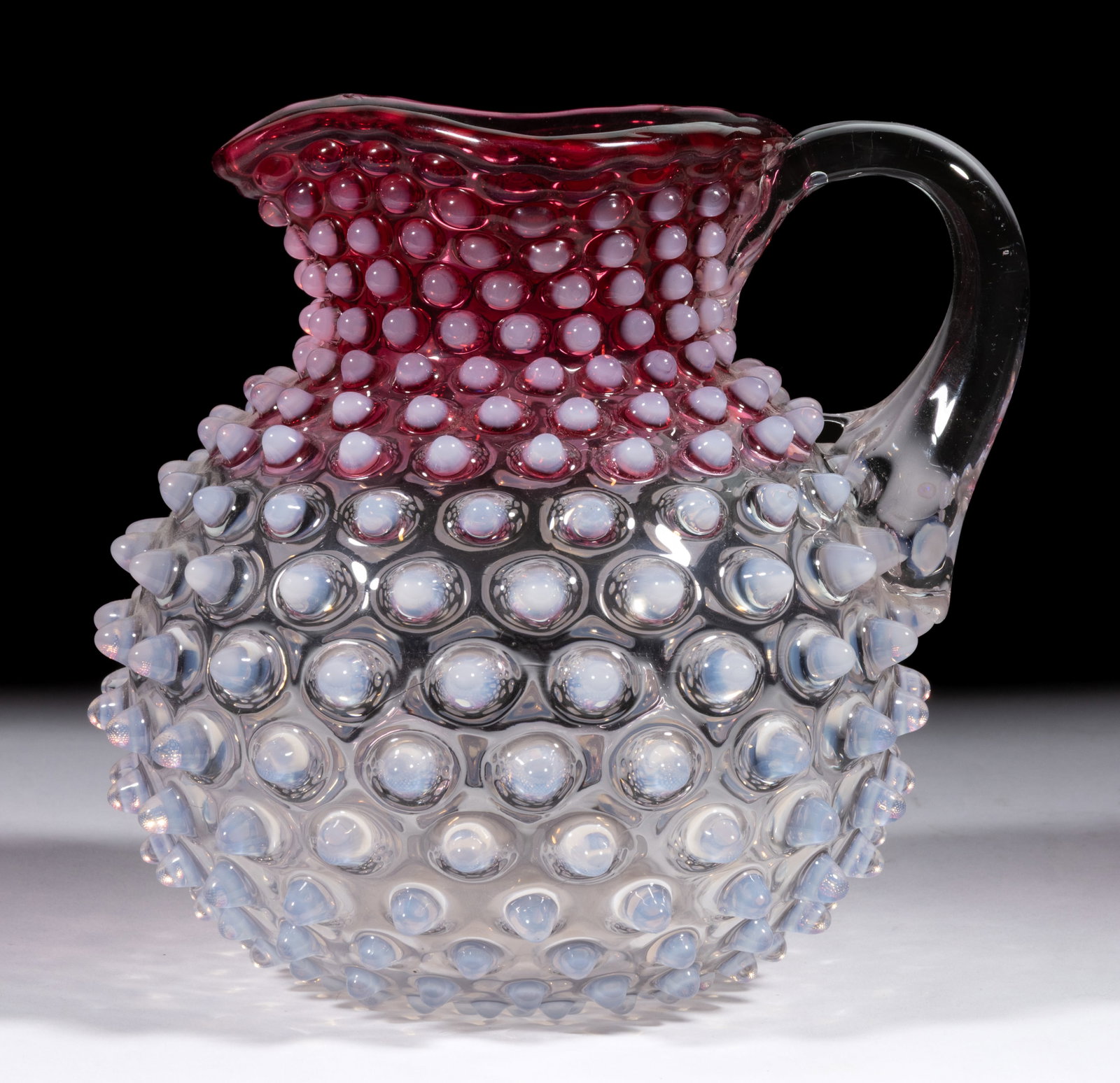 HOBBS NO. 323 DEW DROP / HOBNAIL NO. 4 JUG / PITCHER: HOBBS NO. 323 DEW DROP / HOBNAIL NO. 4 JUG / PITCHER, rubina opalescent, square rim, applied colorless handle, and polished pontil mark. Hobbs, Brockunier & Co. Pattern introduced in 1886. 7"