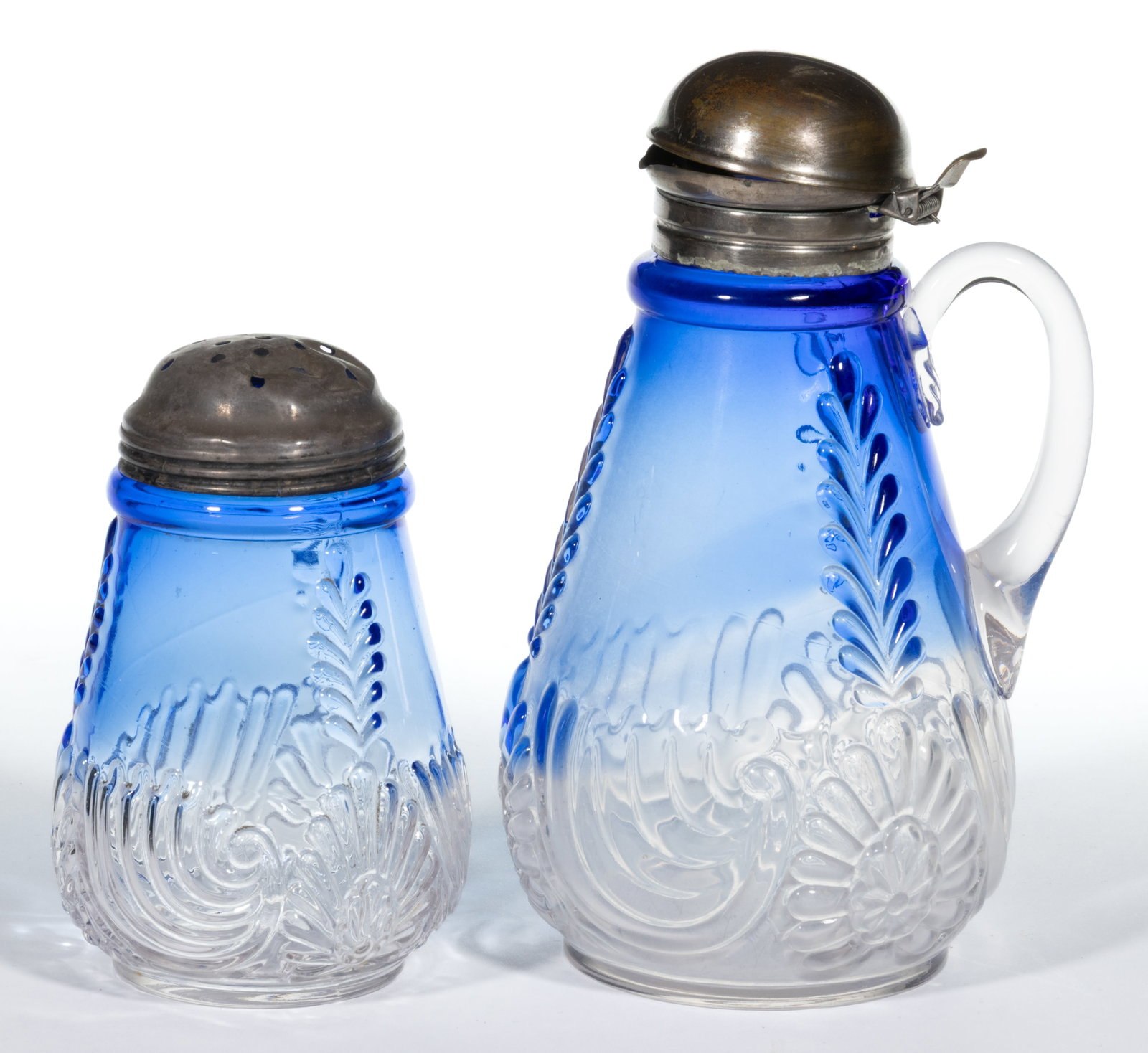 MEDALLION SPRIG TABLE ARTICLES, LOT OF TWO: MEDALLION SPRIG TABLE ARTICLES, LOT OF TWO, blue shaded to colorless, comprising a syrup pitcher with applied handle and sugar shaker, both with period lids. West Virginia Glass Co. Circa 1894. 4