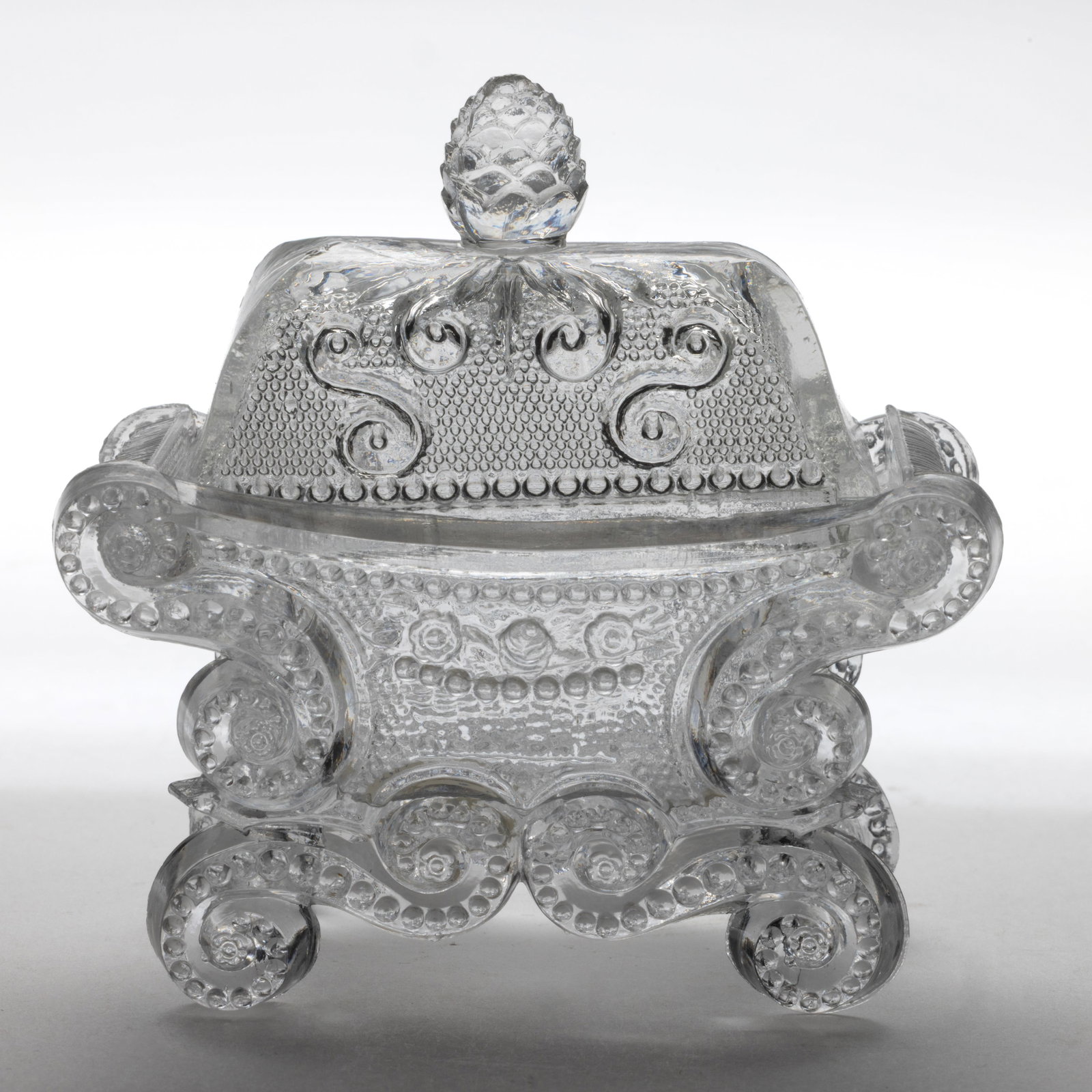 CD-2A COVERED BEADED SCROLL AND BASKET OF FLOWERS PRESSED SALT: CD-2A COVERED BEADED SCROLL AND BASKET OF FLOWERS PRESSED SALT, colorless, raised on four scrolled feet, cover with pine cone finial and beads on rim interior arranging 10 x 20 x 10 x 20, base rays wi