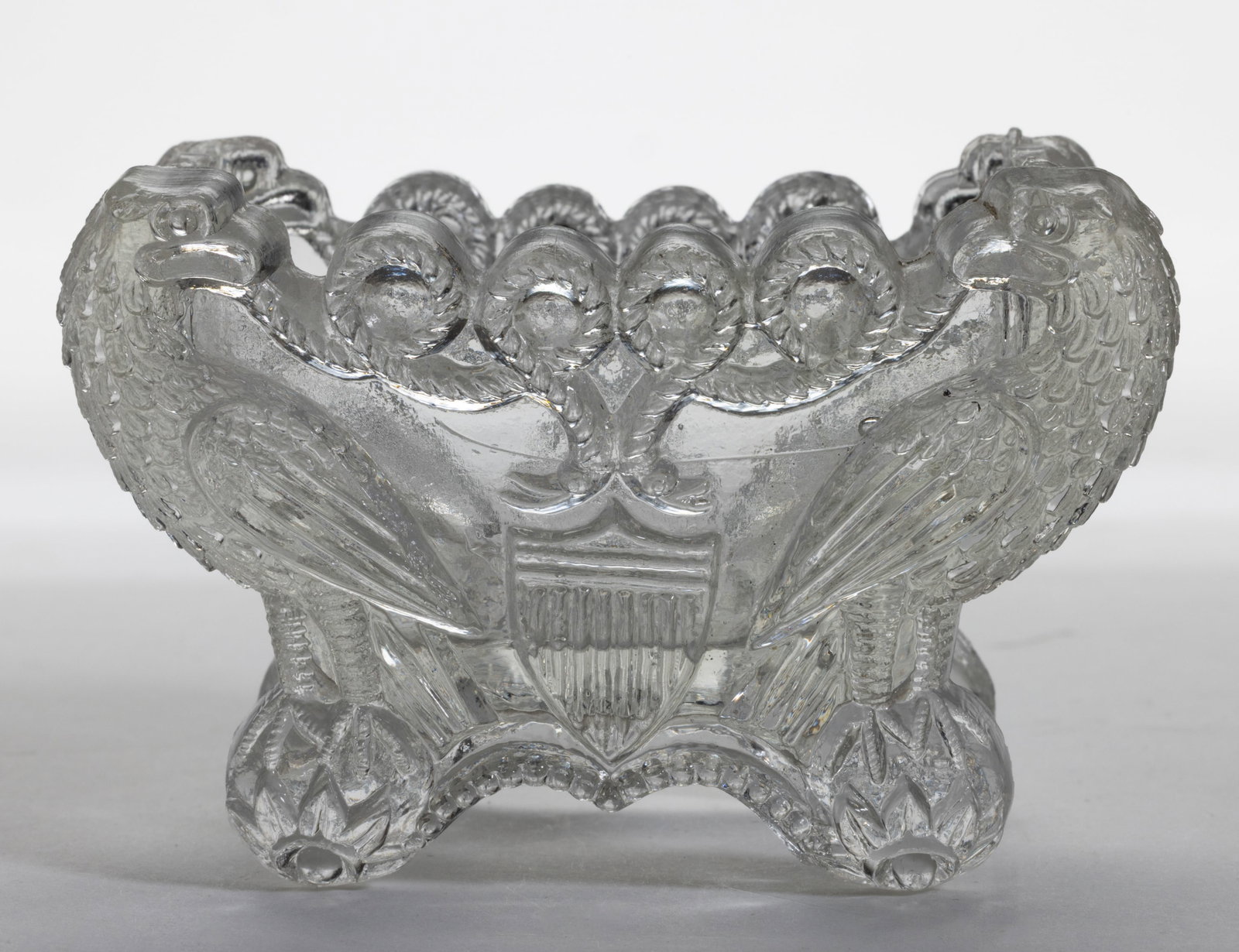 EE-3B EAGLE AND SHIELD PRESSED OPEN SALT: EE-3B EAGLE ADN SHIELD PRESSED OPEN SALT, colorless, raised on four feet. Scarce. Boston & Sandwith Glass Co. 1830-1845. 2 1/8" H, 2" x 3 1/4". Literature: Neal - Pressed