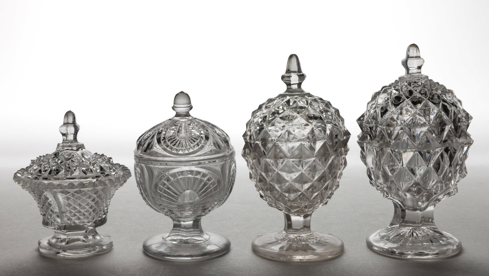 FLINT AND NON-FLINT EAPG COVERED SALTS, LOT OF FOUR: FLINT AND NON-FLINT EAPG COVERED SALTS, LOT OF FOUR, colorless, including two Sawtooth examples and a Serrated Magnet example. Second half 19th/first quarter 20th century. 3 1/2" to 5" H. Pr