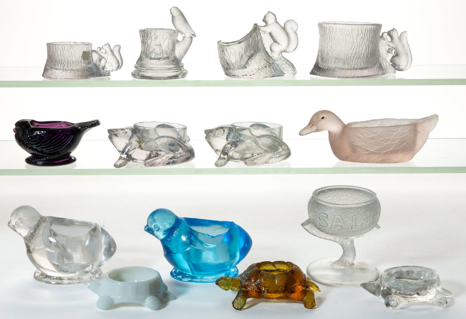 ASSORTED PRESSED NOVELTY GLASS OPEN SALTS, LOT OF 14: ASSORTED PRESSED NOVELTY GLASS OPEN SALTS, LOT OF 14, including colorless, light blue, amethyst, and amber, forms comprising a Gillinder Squirrel on Stump, a Fostoria bird, two U.S. Glass Co. &qu