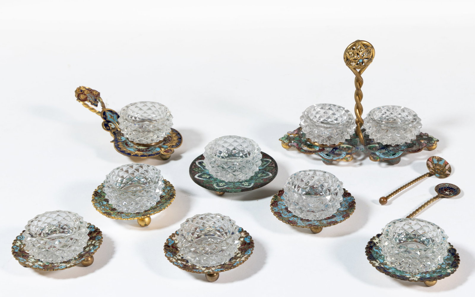 FRENCH CUT GLASS AND ENAMELED OPEN SALTS, LOT OF TEN: FRENCH CUT GLASS AND ENAMELED OPEN SALTS, LOT OF TEN, comprising nine diminutive colorless pressed-diamond salt dishes, each fitted in an enamel-decorated brass stand, two having a spoon. France.