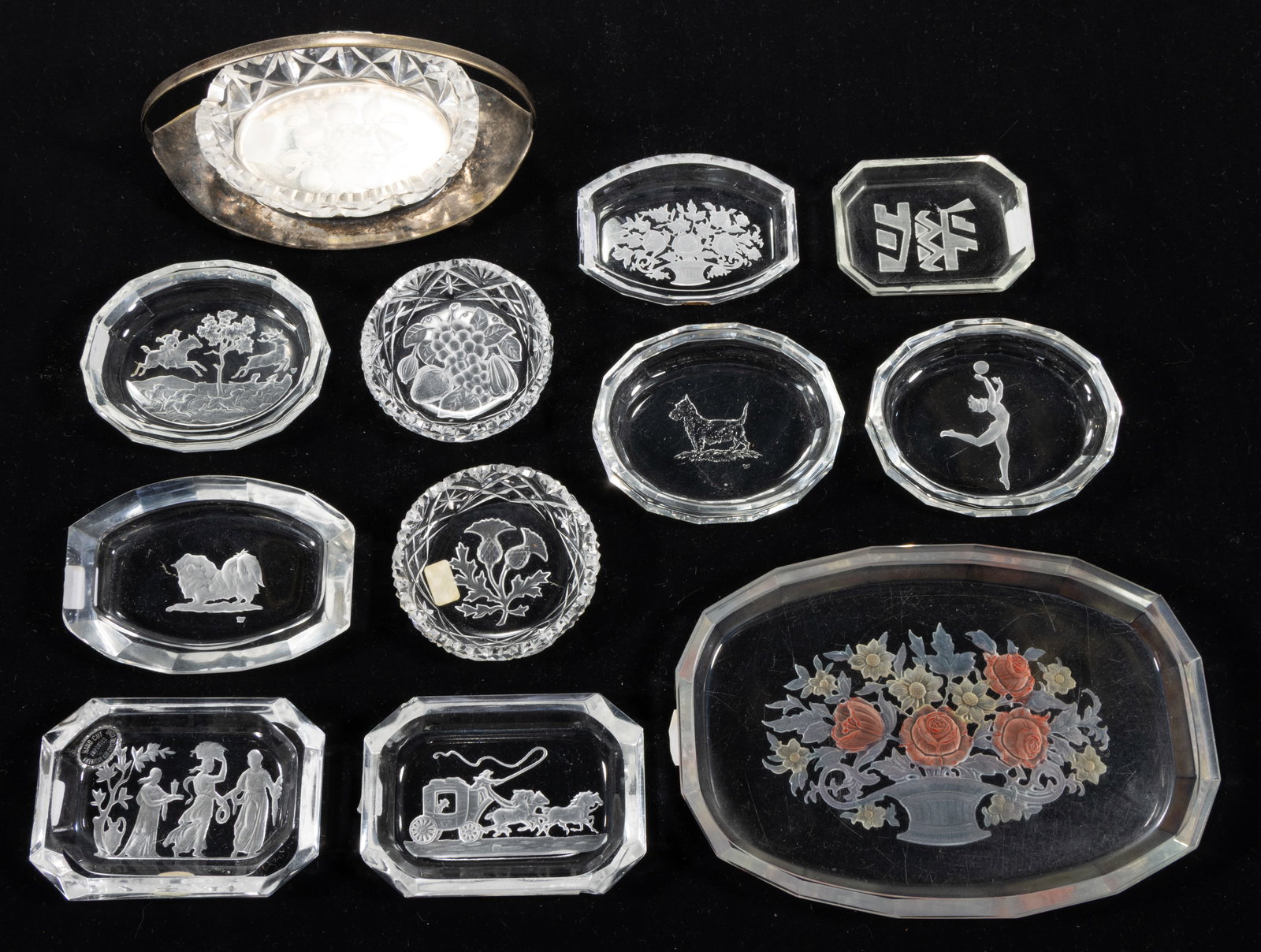 INTAGLIO GLASS ASHTRAYS, LOT OF 12: INTAGLIO GLASS ASHTRAYS, LOT OF 12, colorless, including two featuring a dog, one an athlete, one a stag hunt, one a horse-drawn carriage, and one a Classical scene, one fitted into a metal stand