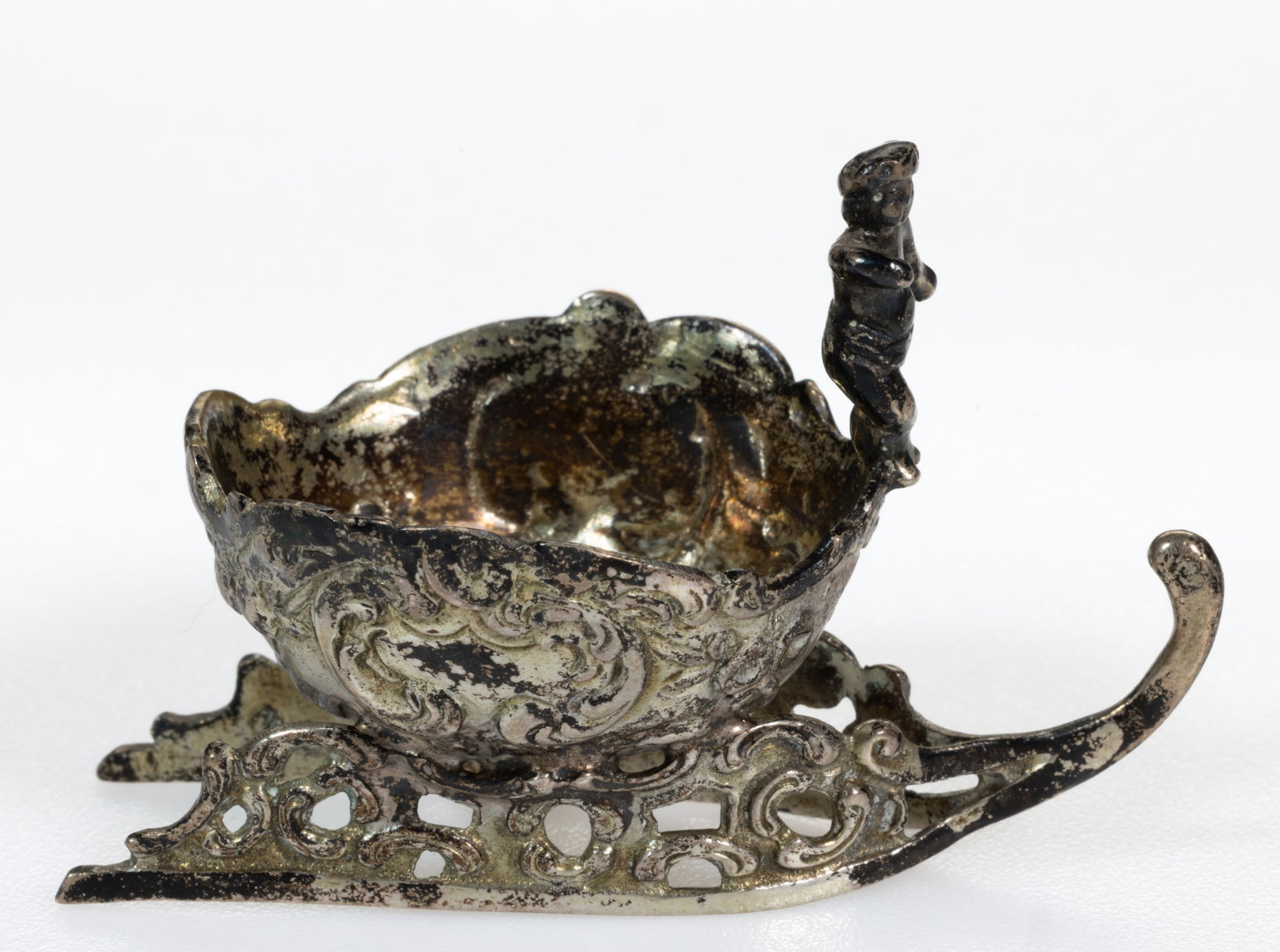 GERMAN, PROBABLY HANAU, FIGURAL SLED 0.800 SILVER OPEN SALT: GERMAN HANAU FIGURAL SLED 0.800 SILVER OPEN SALT, individual sized, having a round well with shaped rim, embellished by scrolls and flower garlands, a figure stands on the rim at the front of the sled