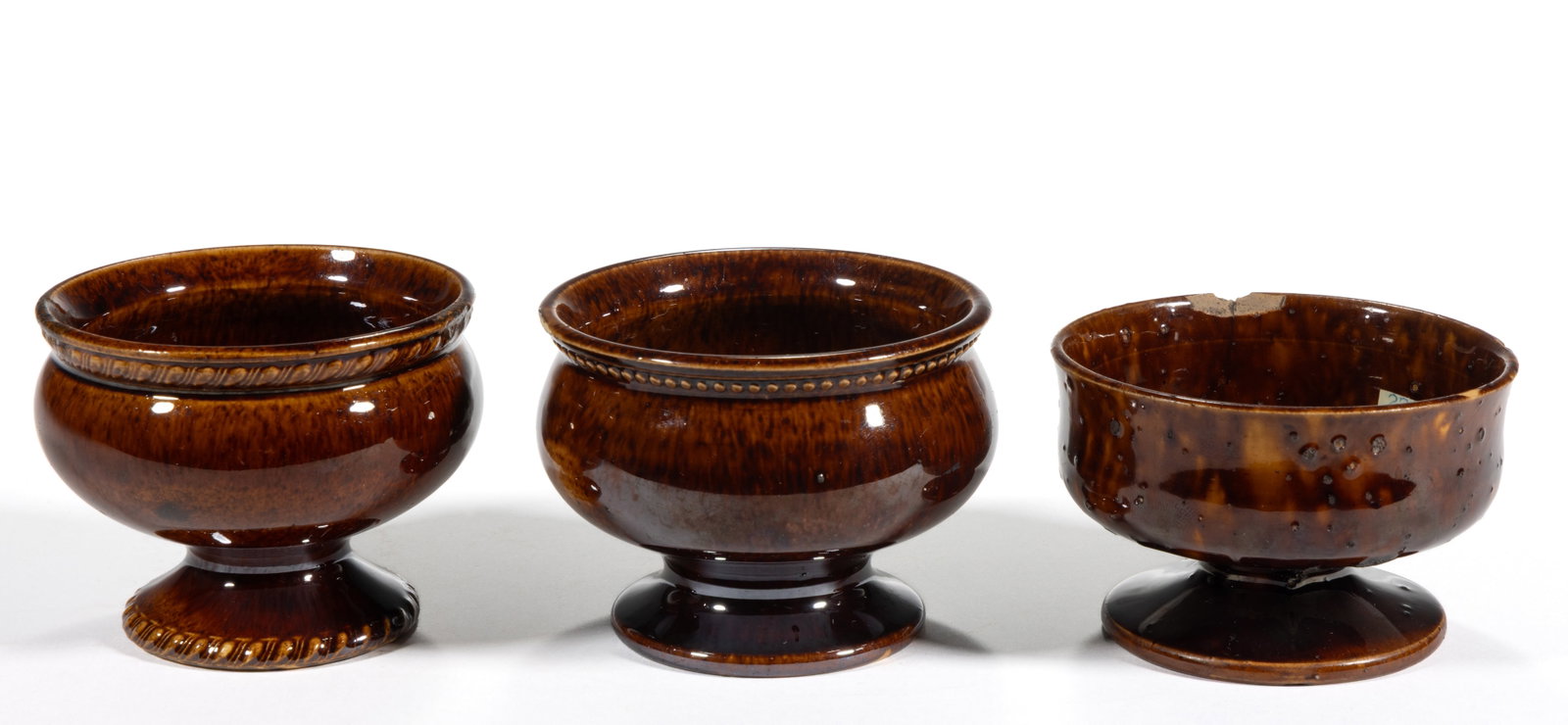 ASSORTED ROCKINGHAM-GLAZED CERAMIC OPEN SALTS, LOT OF THREE: ASSORTED ROCKINGHAM-GLAZED CERAMIC OPEN SALTS, LOT OF THREE, each of pedestal form, including one example having molded gadroon rim and foot and one example with beaded rim decoration. 19th 