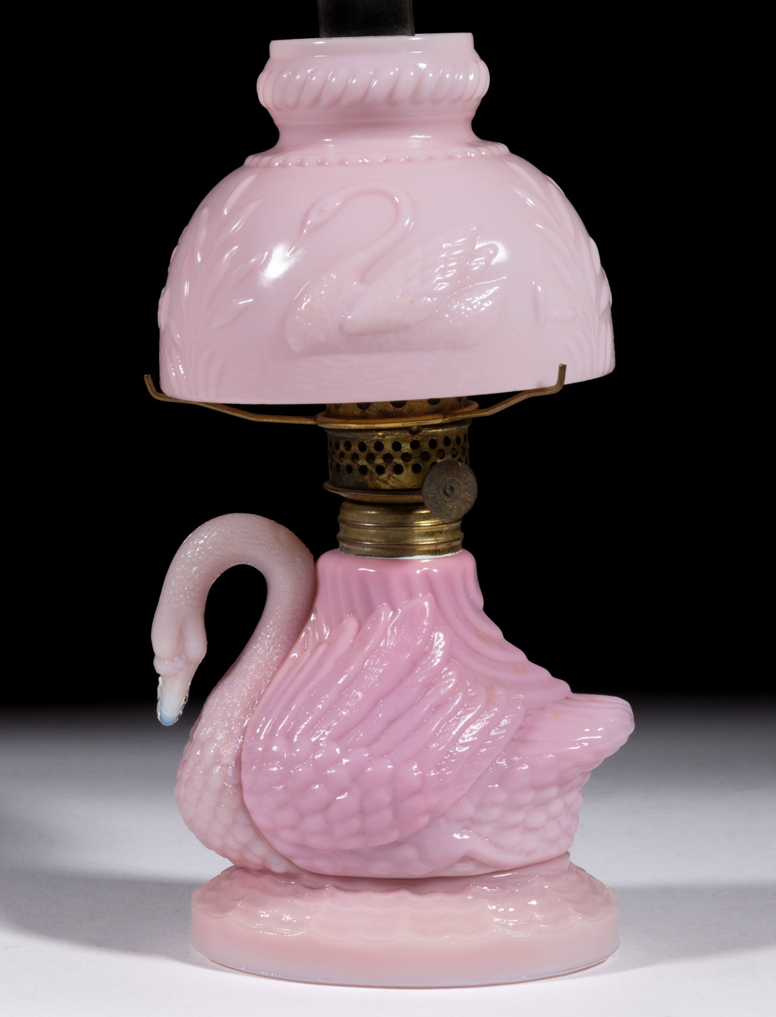 SWAN FIGURAL MINIATURE LAMP: SWAN FIGURAL MINIATURE LAMP, opaque pink with slight mottling, neck and head with light opalescence, font raised on an oval base having a plain table ring, matching patterned pale 