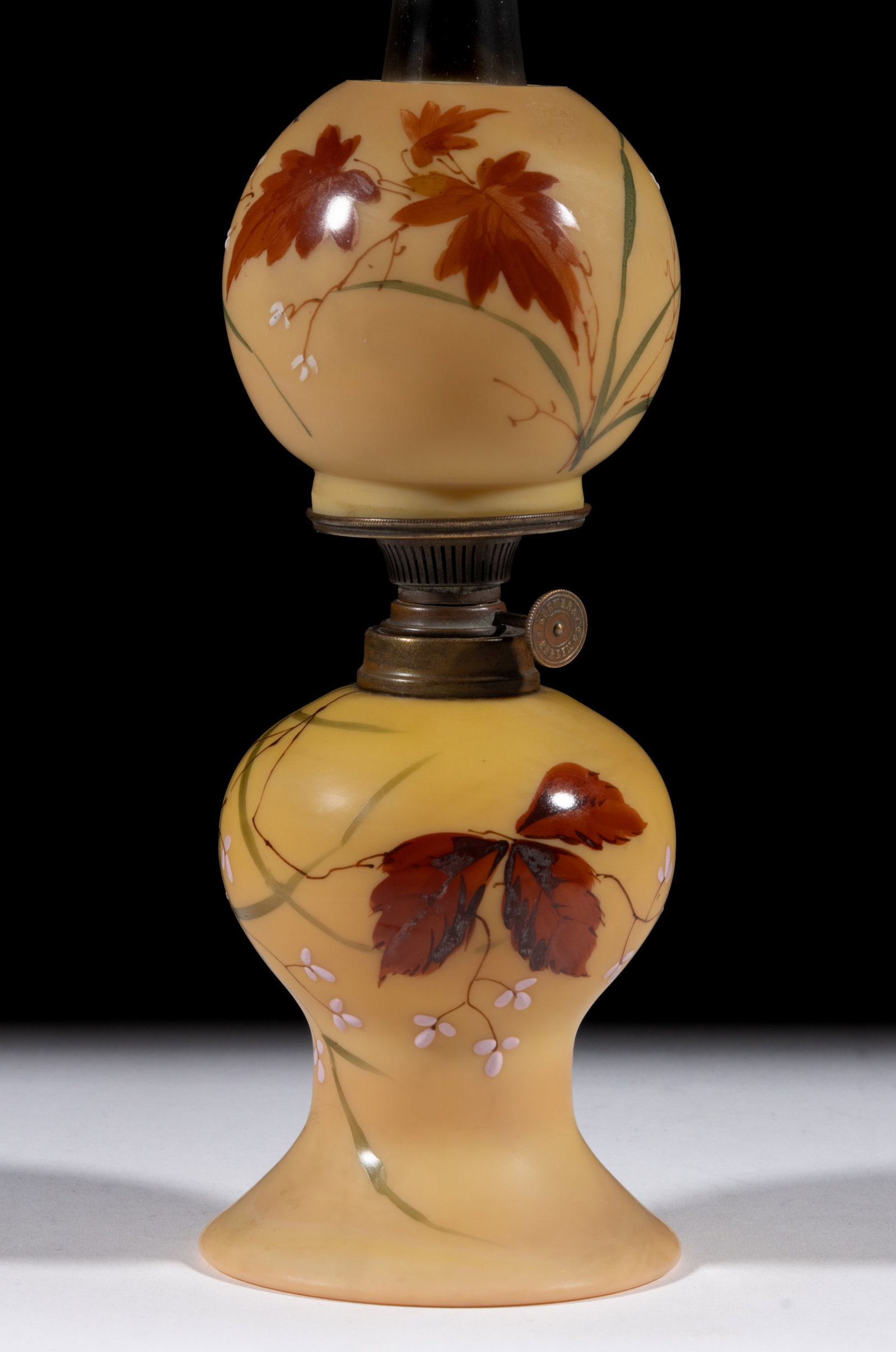VICTORIAN ENAMEL DECORATED BURMESE GLASS MINIATURE LAMP: VICTORIAN ENAMEL DECORATED BURMESE GLASS MINIATURE LAMP, Burmese with plush finish and polychrome decoration of fall foliage and pale pink raised flowers, globular-form font with pedestal and flared c