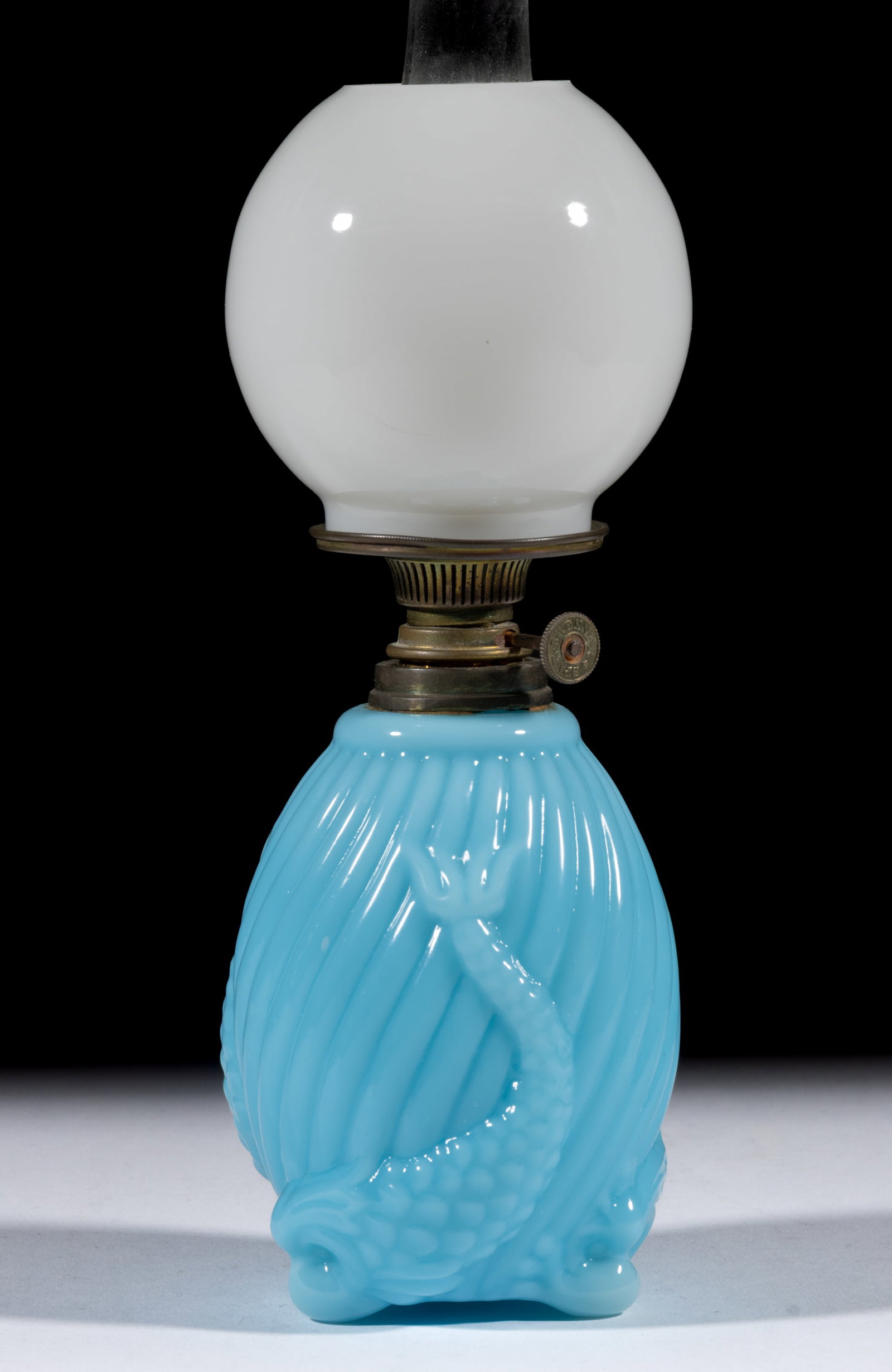 UNLISTED FISH AND SWIRLED RIB FIGURAL OPAQUE GLASS MINIATURE LAMP: UNLISTED FISH AND SWIRLED RIB FIGURAL OPAQUE GLASS MINIATURE LAMP, opaque blue, elongated-form with swirls of ribs, raised on three short feet depicting fish heads and tails extending into font body, 