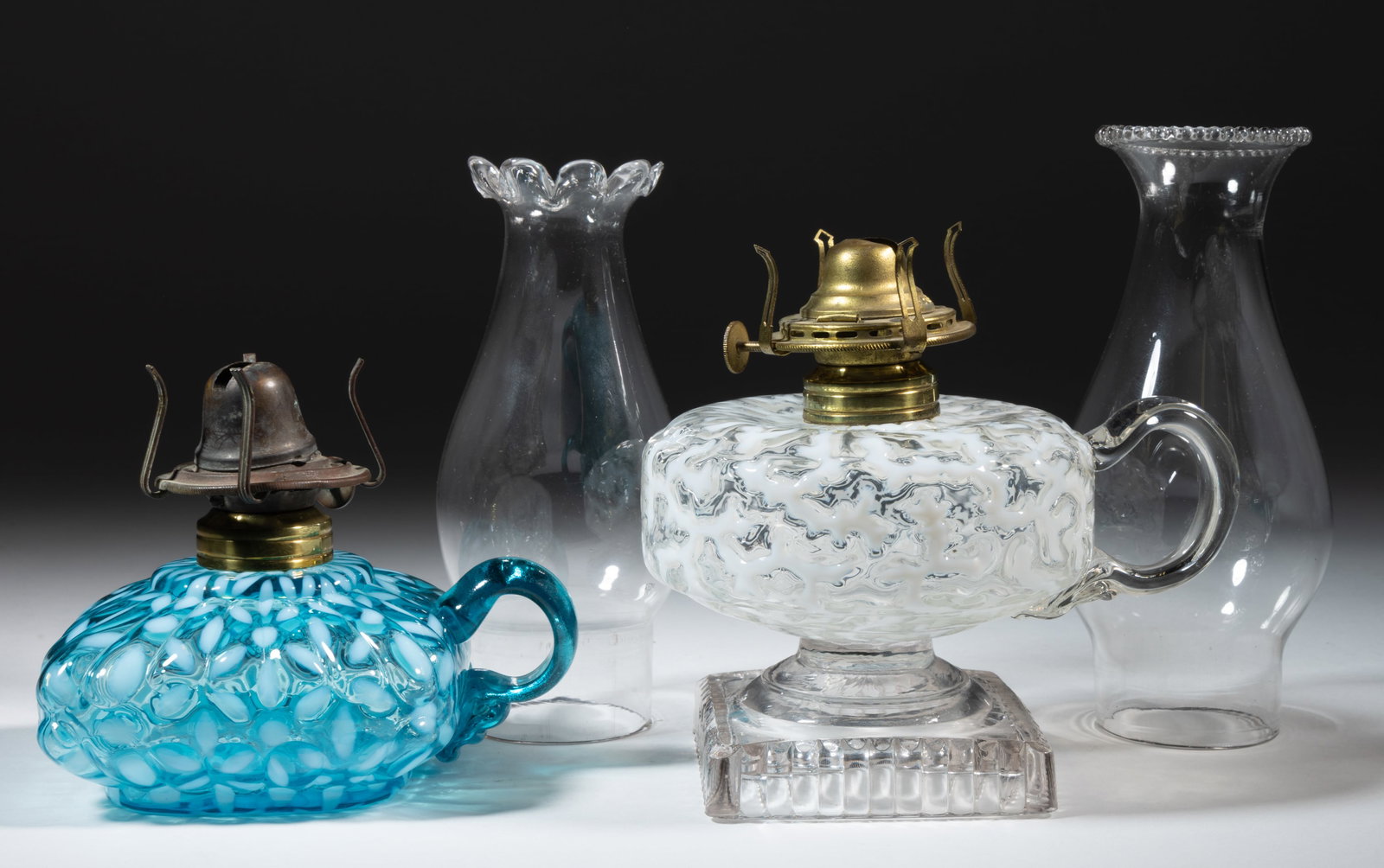 ASSORTED HOBBS KEROSENE FINGER LAMPS, LOT OF TWO: ASSORTED HOBBS KEROSENE FINGER LAMPS, LOT OF TWO, comprising of a Coral Reef/Seaweed example, having a Crystal/colorless opalescent font, colorless stem and ribbed foot, applied colorless handle 