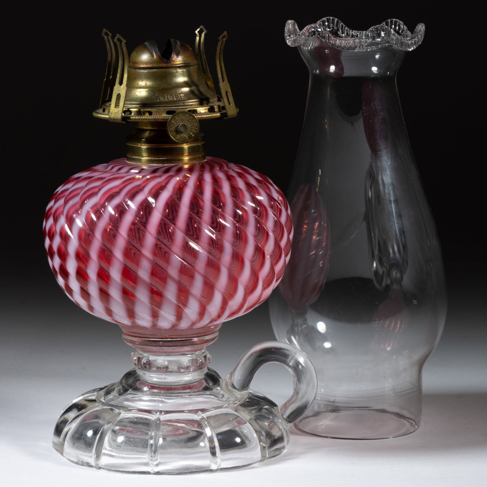 SHELDON SWIRL KEROSENE FOOTED FINGER LAMP: SHELDON SWIRL KEROSENE FOOTED FINGER LAMP, cranberry opalescent Reverse Swirl font, colorless base with molded ring handle, No. 1 Taplin-Brown collar. Fitted with a period setup comprising a No. 