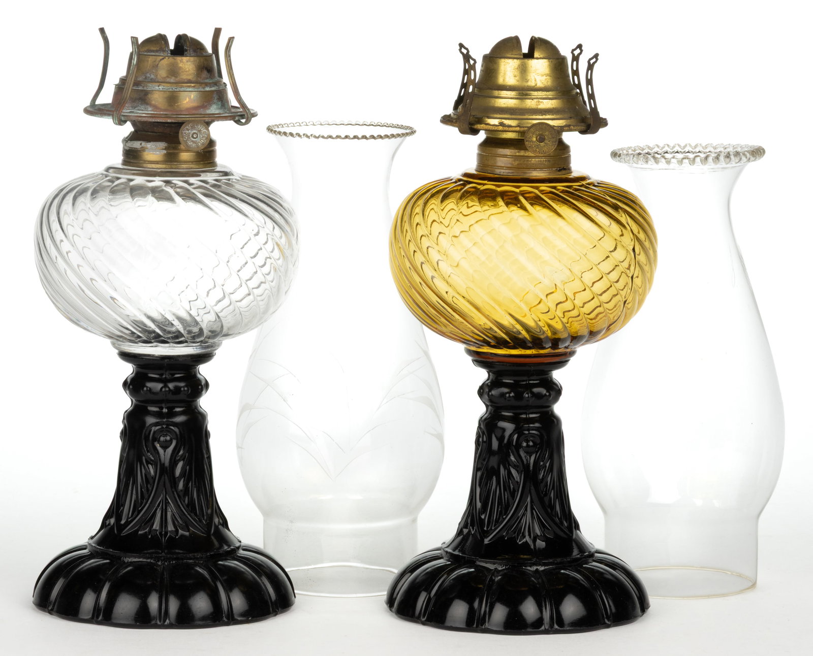 SHELDON SWIRL KEROSENE STAND LAMPS, LOT OF TWO: SHELDON SWIRL KEROSENE STAND LAMPS, LOT OF TWO, comprising of a colorless font and a honey amber font, each with an opaque black base; each with a No. 2 Taplin-Brown collar having patent information. 