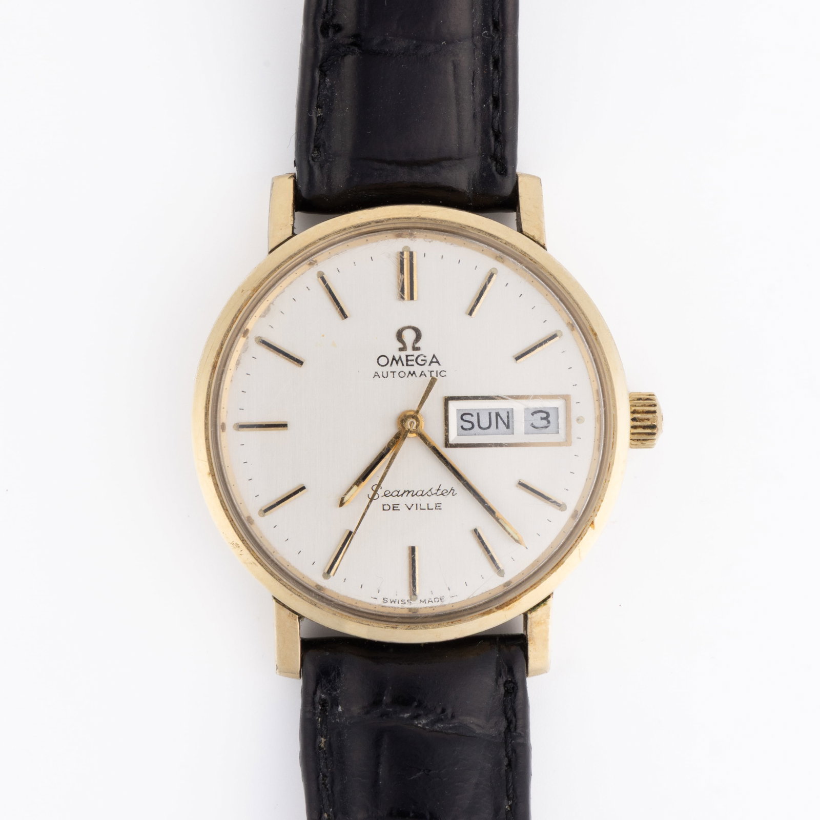 VINTAGE OMEGA SEAMASTER DEVILLE WRIST WATCH: VINTAGE OMEGA SEAMASTER DEVILLE WRIST WATCH, silver-colored dial with gold and black bar indices with day and date aperture at the 3 position, housed in a round yellow gold-colored case with a black l