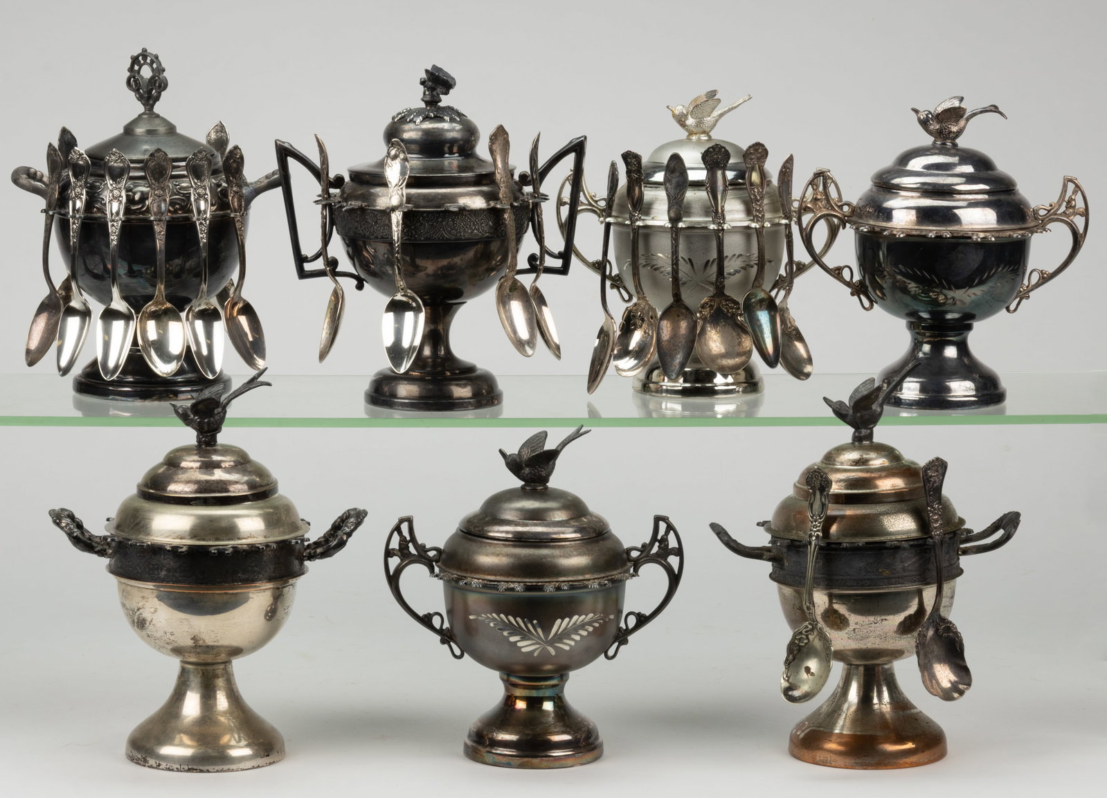 ASSORTED SILVER-PLATED COVERED SPOONERS / SUGAR BOWLS, LOT OF SEVEN: ASSORTED SILVER-PLATED COVERED SPOONERS / SUGAR BOWLS, LOT OF SEVEN, each piece with round bowl having two handles and a group of spoon holders around the shoulders, raised on a stemmed foot, topped