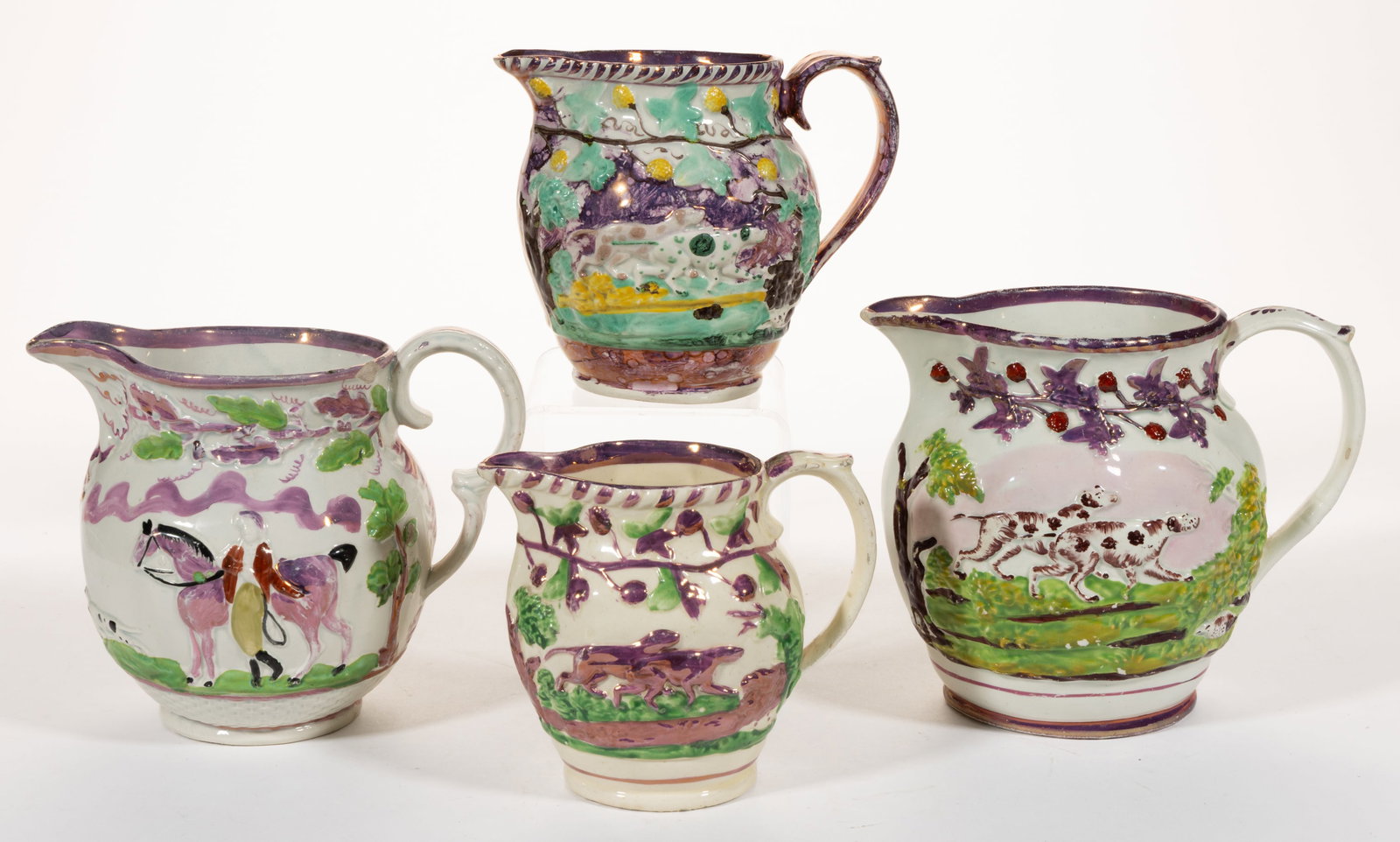 BRITISH RELIEF-MOLDED PINK LUSTRE HUNTING MOTIF CERAMIC JUGS / PITCHERS, LOT OF FOUR: BRITISH RELIEF-MOLDED PINK LUSTRE HUNTING MOTIF CERAMIC JUGS / PITCHERS, LOT OF FOUR, each having polychrome hand-painted decorations, comprising one example depicting a rider with horse to each side 