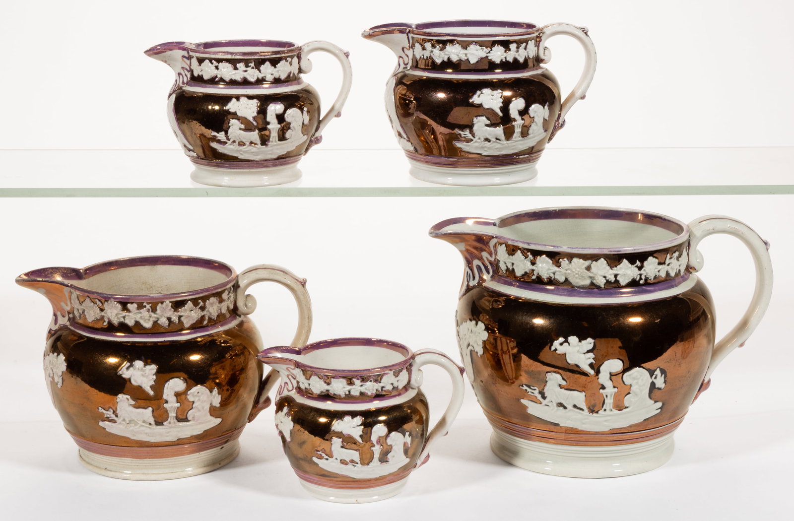 BRITISH LUSTRE-DECORATED CERAMIC GRADUATED JUGS / PITCHERS, ASSEMBLED SET OF FIVE: BRITISH LUSTRE-DECORATED CERAMIC GRADUATED JUGS / PITCHERS, ASSEMBLED SET OF FIVE, each having white sprig decorations featuring neoclassical scenes on copper lustre ground including one side featurin