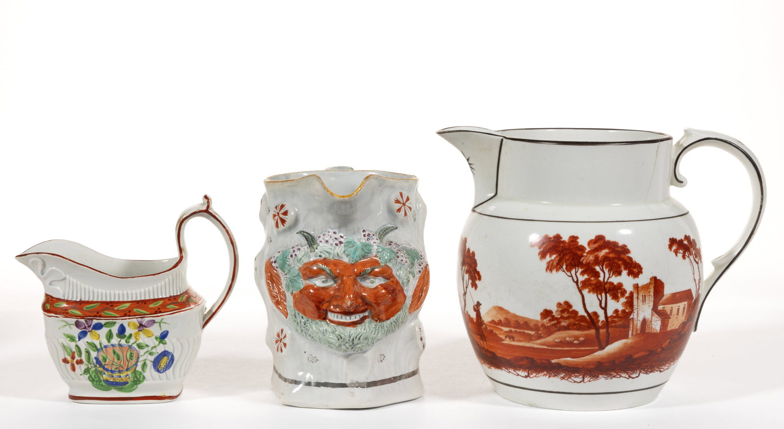 BRITISH HAND-PAINTED CERAMIC JUGS / PITCHERS, LOT OF THREE: BRITISH HAND-PAINTED CERAMIC JUGS / PITCHERS, LOT OF THREE, comprising a molded Bacchus satyr example with silver lustre accents depicting a grinning horned face, a red hand-painted bulbous-form examp