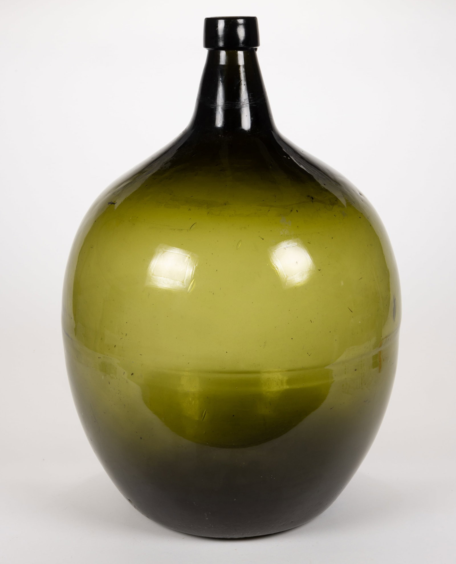 FREE-BLOWN GLASS DEMIJOHN / LARGE UTILITY BOTTLE: FREE-BLOWN GLASS DEMIJOHN / LARGE UTILITY BOTTLE, dark olive green, probably six- or seven-gallon size, globular form with short neck and applied sloping mouth, concave base with rough pontil mark. Am