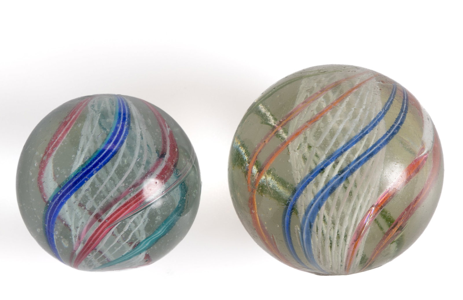 ANTIQUE TRANSPARENT SWIRL LATTICINIO CORE GLASS MARBLES, LOT OF TWO: ANTIQUE TRANSPARENT SWIRL LATTICINIO CORE GLASS MARBLES, LOT OF TWO, each having white latticinio core surrounded by multicolored striped ribbons or threads. Various makers. Late 1