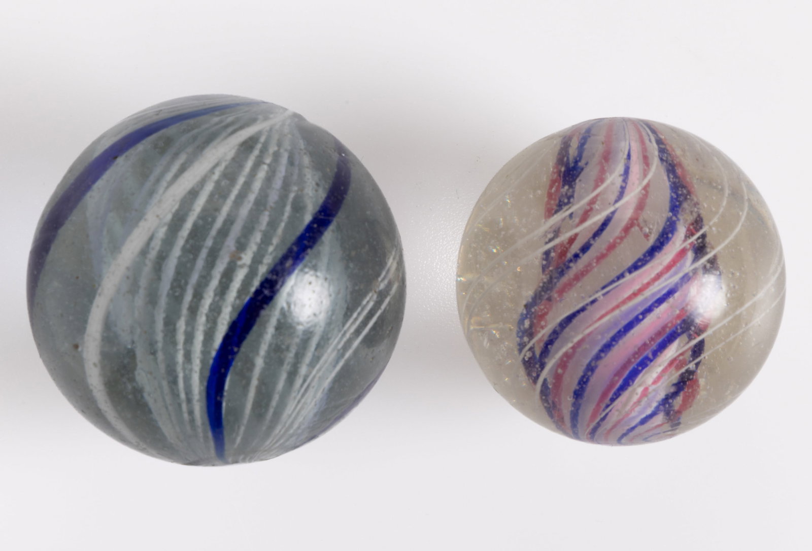 ANTIQUE TRANSPARENT SWIRL GLASS MARBLES, LOT OF TWO: ANTIQUE TRANSPARENT SWIRL GLASS MARBLES, LOT OF TWO, comprising one with white latticinio core surrounded by blue and white alternating ribbons and threads, and one with a solid red, white, and blue&n