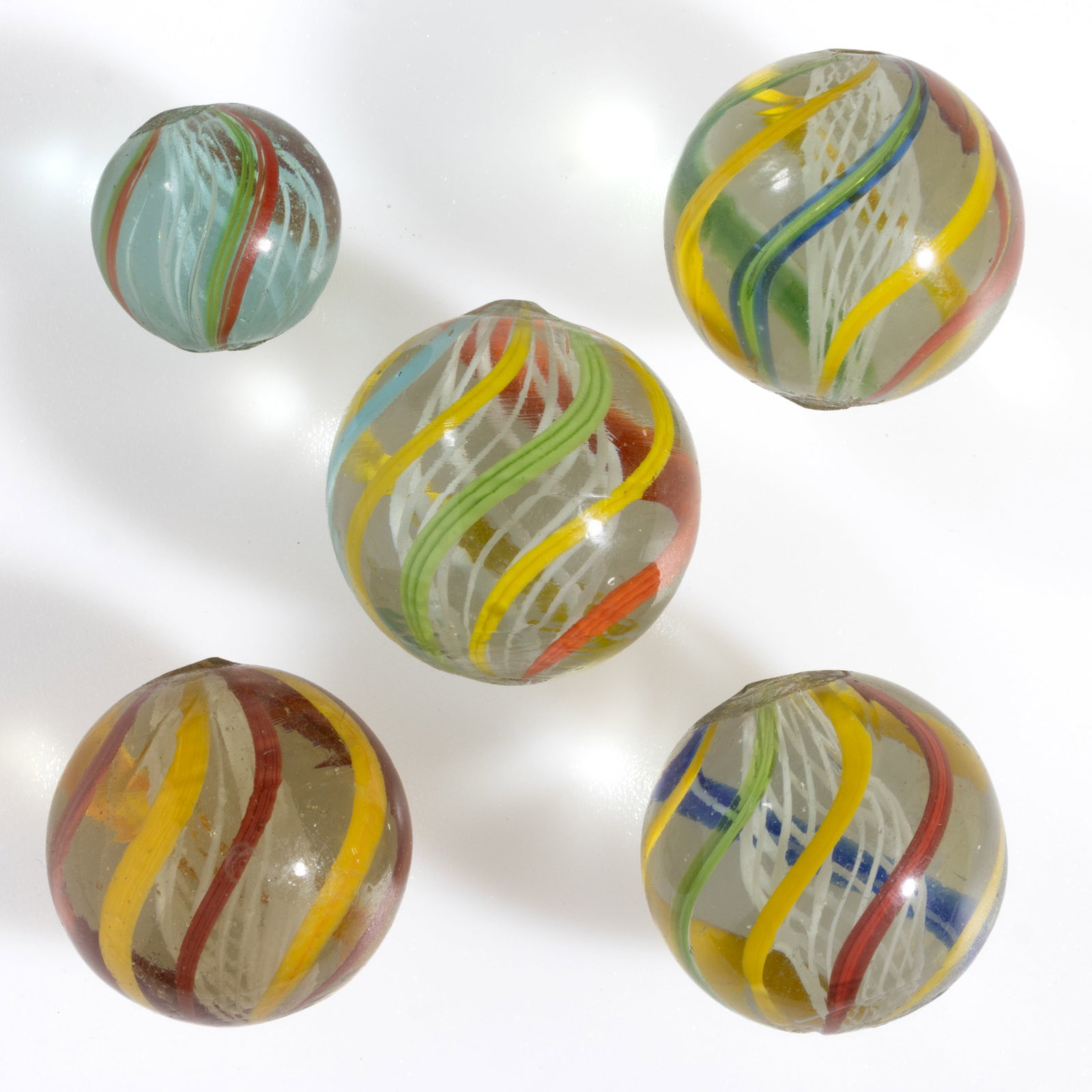 ANTIQUE TRANSPARENT SWIRL LATTICINIO CORE GLASS MARBLES, LOT OF FIVE: ANTIQUE TRANSPARENT SWIRL LATTICINIO CORE GLASS MARBLES, LOT OF FIVE, each having a white latticinio core surrounded by exterior ribbons in various colors. Various makers. Late 19th/early 20th