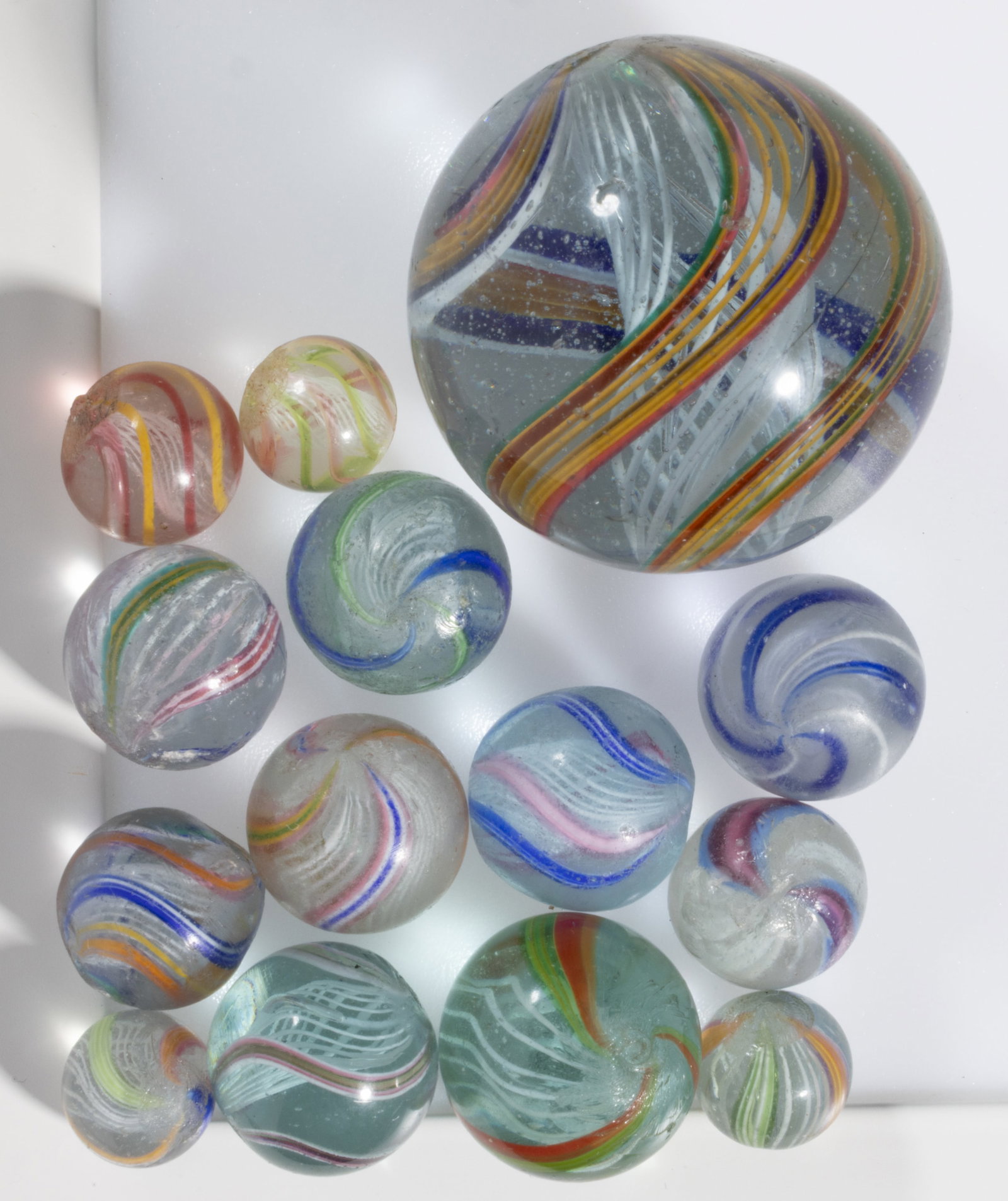 ANTIQUE TRANSPARENT SWIRL LATTICINIO CORE GLASS MARBLES, LOT OF 14: ANTIQUE TRANSPARENT SWIRL LATTICINIO CORE GLASS MARBLES, LOT OF 14, each having a white latticinio core surround by exterior ribbons in various colors. Various makers. Late 19th/early 20th