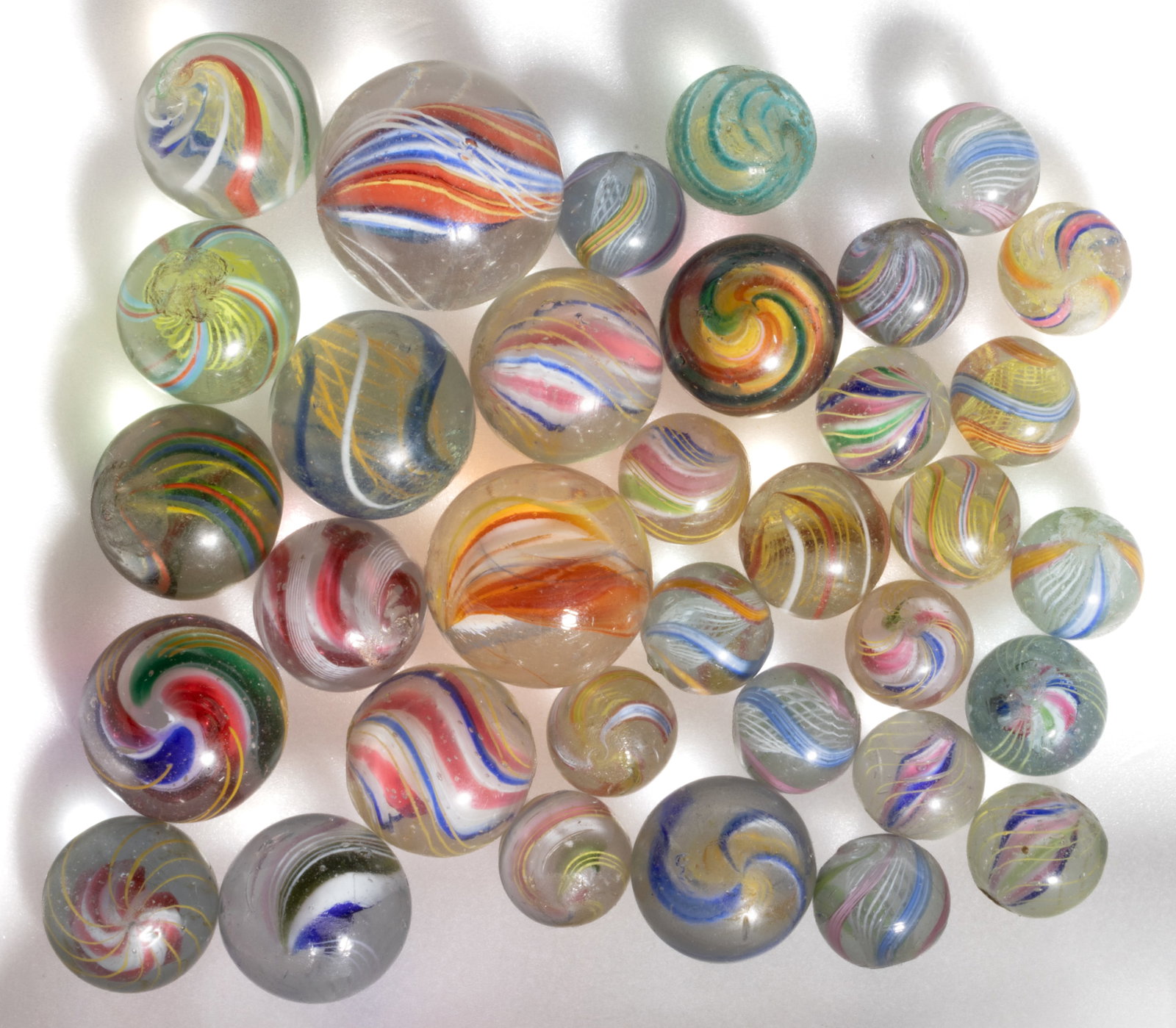 ANTIQUE TRANSPARENT SWIRL GLASS MARBLES, LOT OF 34: ANTIQUE TRANSPARENT SWIRL GLASS MARBLES, LOT OF 34, eighteen having a latticinio core in yellow or white, exterior ribbons of a variety of colors and combinations, and sixteen with interior