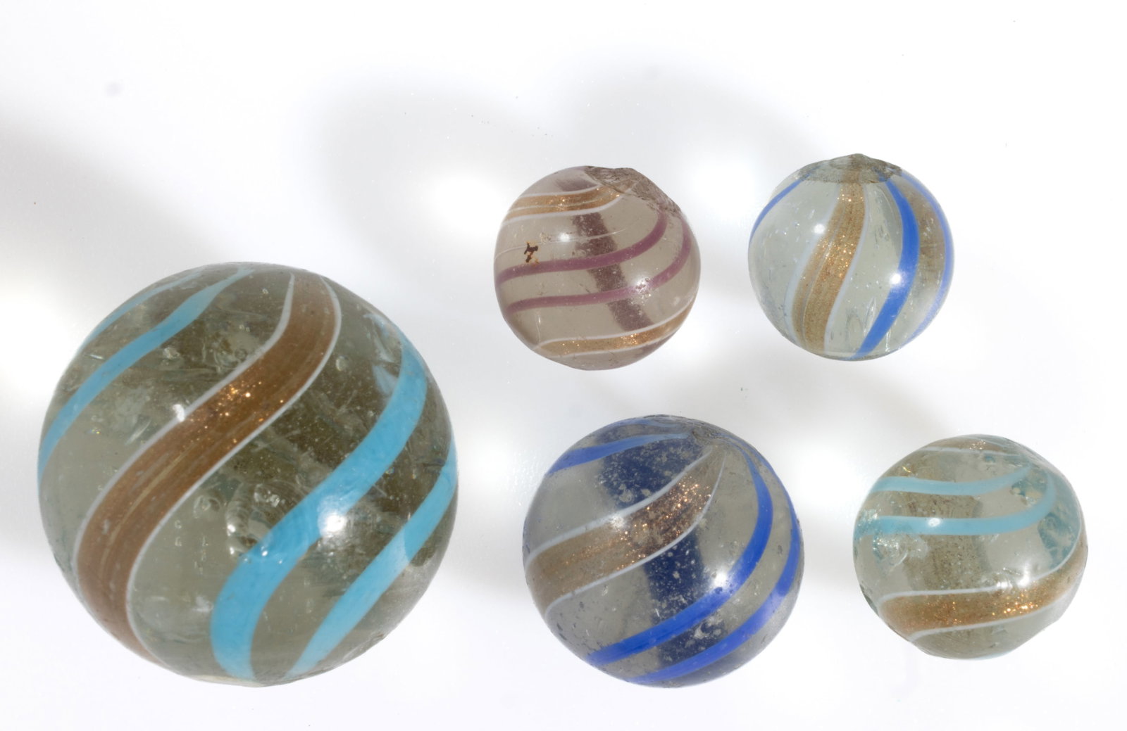 HAND BLOWN LUTZ SWIRL MARBLES, LOT OF FIVE: HAND BLOWN LUTZ SWIRL MARBLES, LOT OF FIVE, colorless base color, comprising four with blue and gold aventurine swirls, and one with purple and gold aventurine swirls, each having rough pontil ma