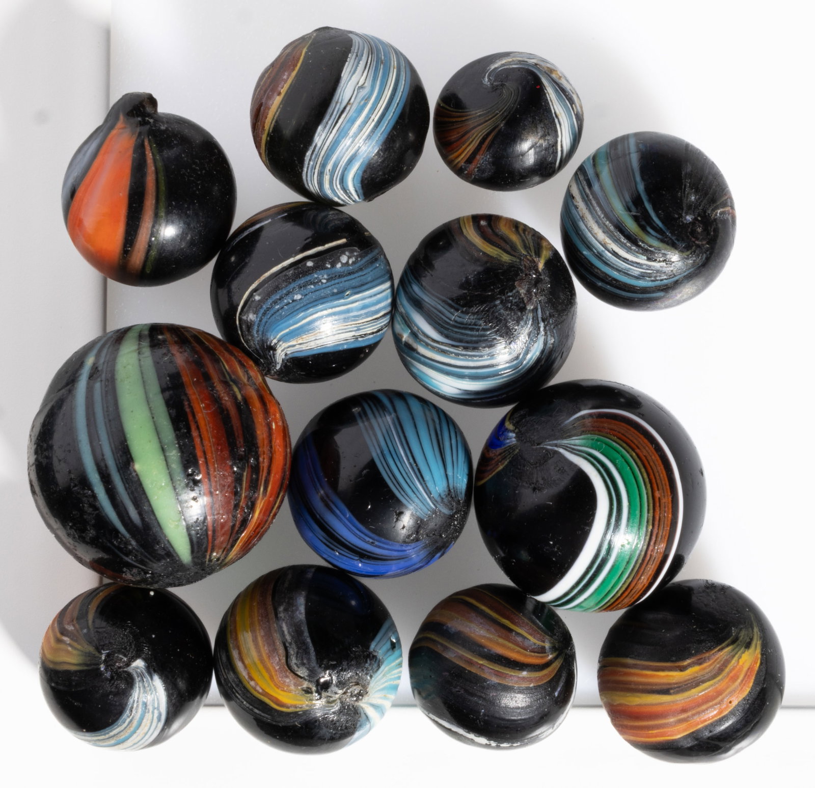 ANTIQUE INDIAN SWIRL MARBLES, LOT OF 13: ANTIQUE INDIAN SWIRL MARBLES, LOT OF 13, each opaque black with varying bands of color. Various makers. Late 19th/early 20th century. 1/2" to 1" D. Provenance: From the collection 