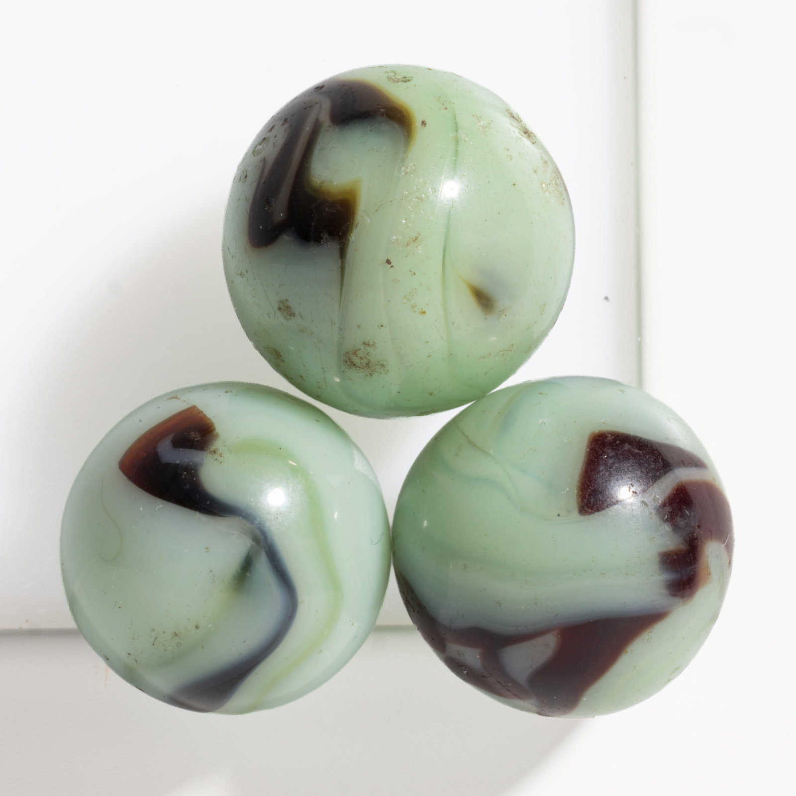 ALLEY AGATE PISTACHIO MACHINE-MADE MARBLES, LOT OF THREE: ALLEY AGATE PISTACHIO MACHINE-MADE MARBLES, LOT OF THREE, green fluorescent (reacts under black light) base color, with dark brown-to-black ribboning decoration. Alley Agate Co. Circa 1935. 5/8&q