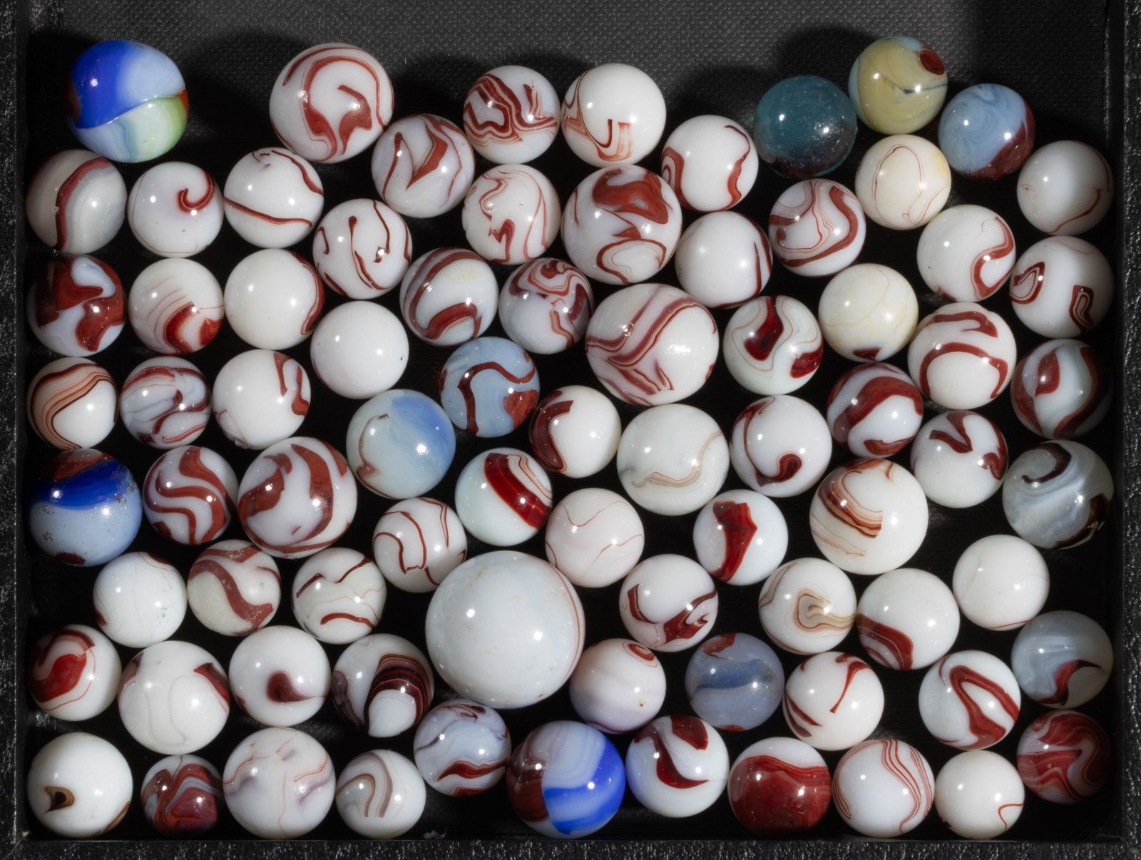 OXBLOOD MACHINE-MADE MARBLES, LOT OF 79: OXBLOOD MACHINE-MADE MARBLES, LOT OF 79, including an ingot. Various makers. Second quarter 20th century. 9/16" to 1" D. Provenance: From the collection of the late Raymond Ga