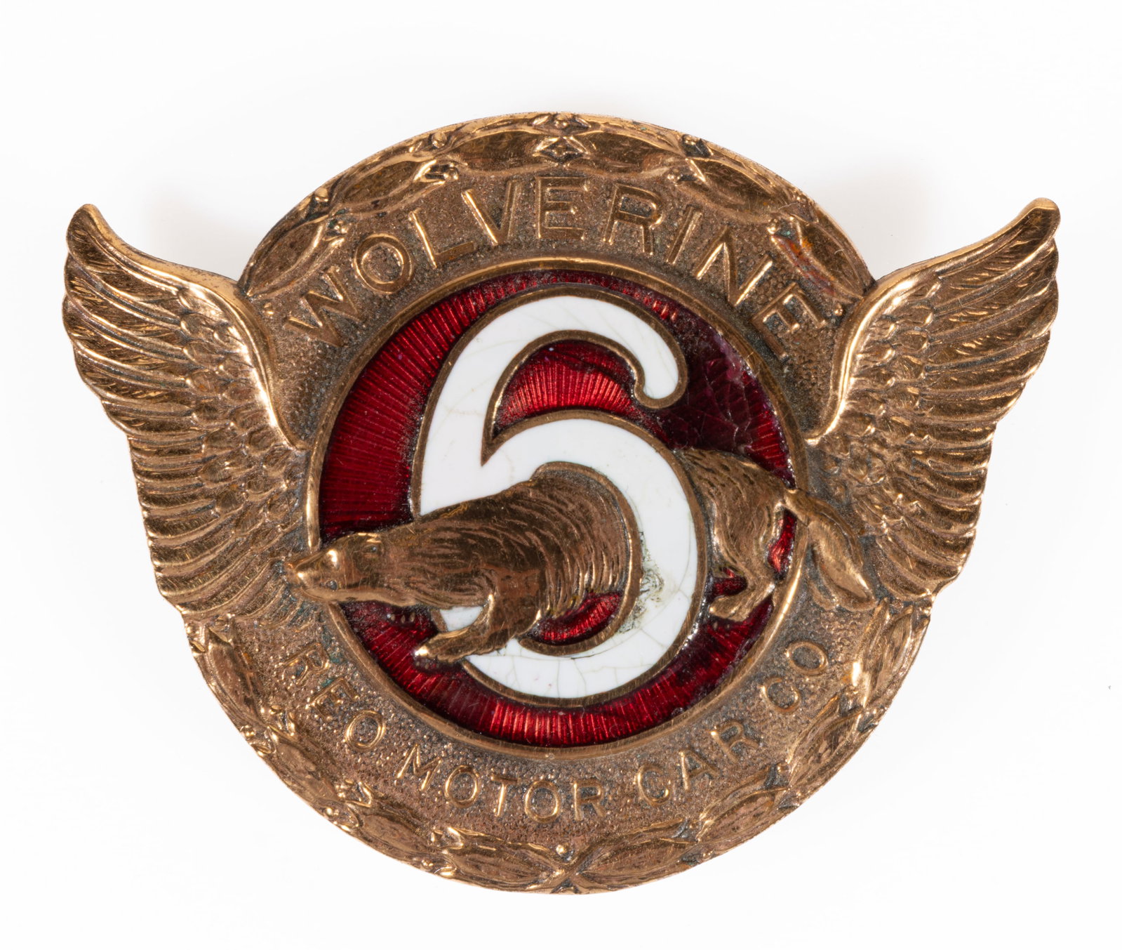 REO MOTOR CAR CO. WOLVERINE AUTOMOBILE / CAR / VEHICLE RADIATOR / GRILL EMBLEM: REO MOTOR CAR CO. WOLVERINE AUTOMOBILE / CAR / VEHICLE RADIATOR / GRILL EMBLEM, polished brass with small wings and ovoid beading to upper and lower edge, center with red enameling and a white enamel 