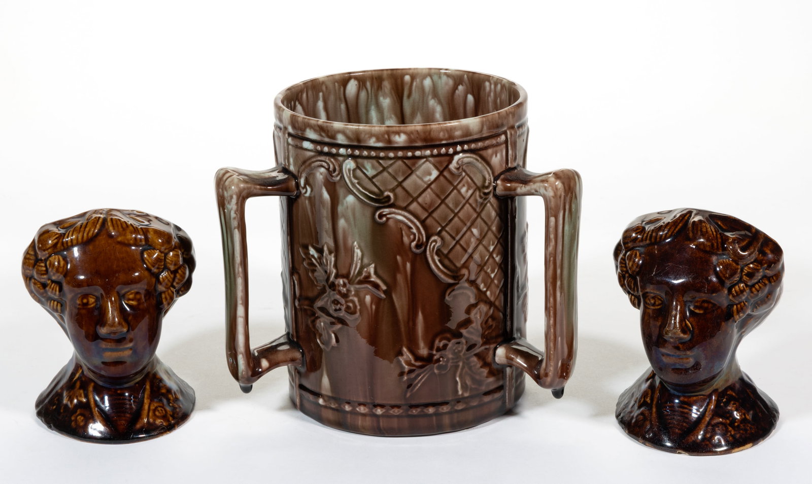 ASSORTED POTTERY ARTICLES, LOT OF THREE: ASSORTED POTTERY ARTICLES, LOT OF THREE, comprising a pair of Rockingham-glazed figural stove rests depicting a woman's head and a majolica cylindrical-form mug with three-handles having mottled