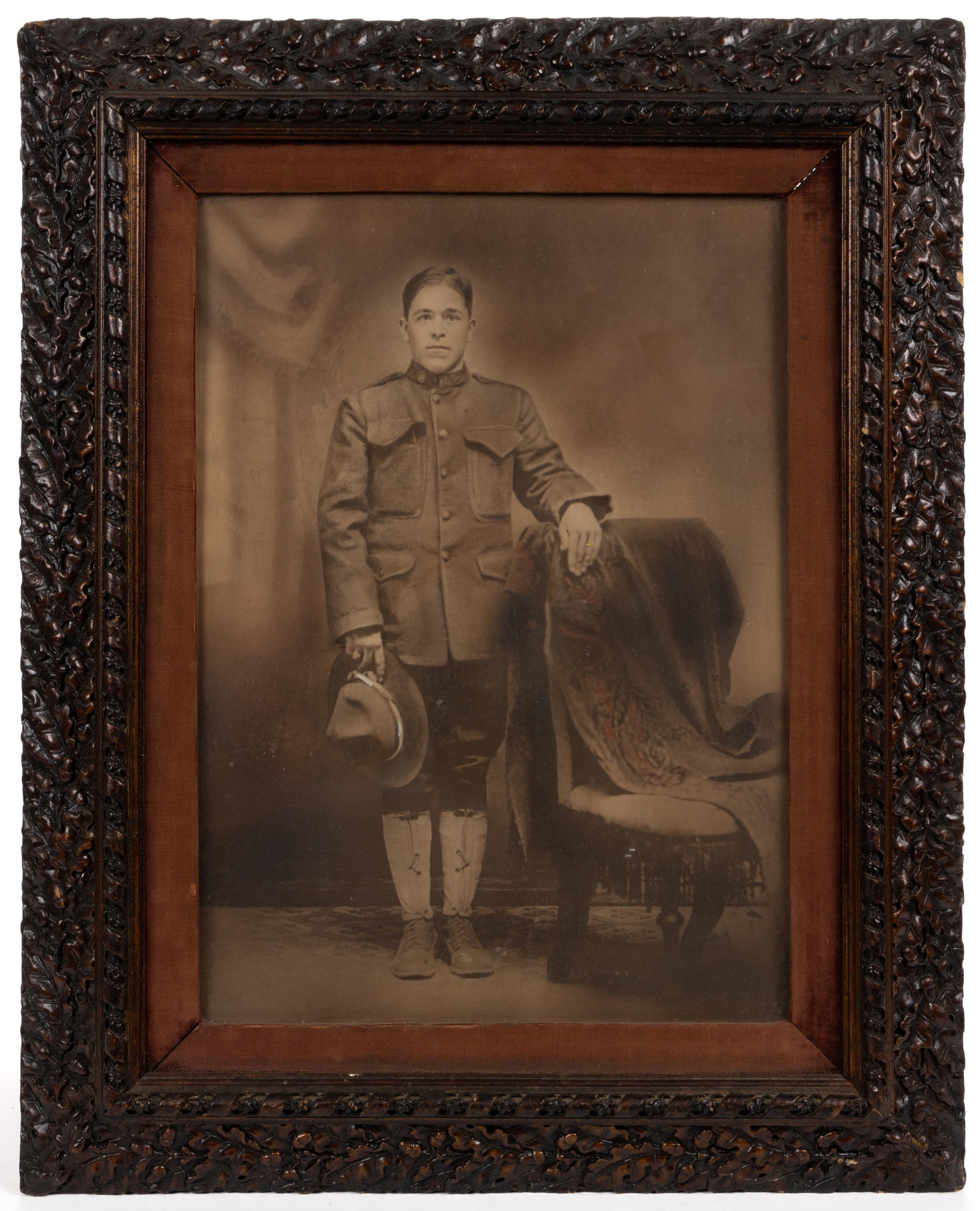 AMERICAN WORLD WAR I / WWI PHOTOGRAPH OF A SOLDIER IN OAK LEAF FRAME: AMERICAN WORLD WAR I / WWI PHOTOGRAPH OF A SOLDIER IN OAK LEAF FRAME, a full-length depiction of a young soldier with a hand-colored wedding band and hand-colored highlights to his hat. Housed under w
