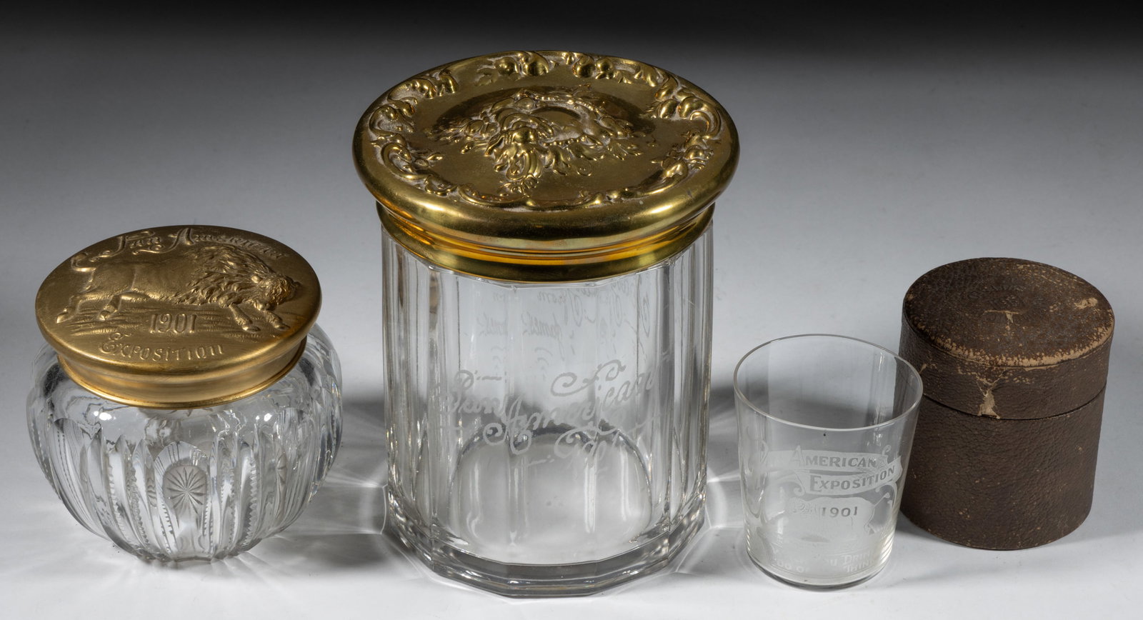 PAN-AMERICAN EXPOSITION / BUFFALO GLASS SOUVENIR ARTICLES, LOT OF THREE: PAN-AMERICAN EXPOSITION / BUFFALO GLASS SOUVENIR ARTICLES, LOT OF THREE, comprising two tobacco jars or humidors, the smaller of cut glass with a gilt-brass cover with a central embossed buffalo lette